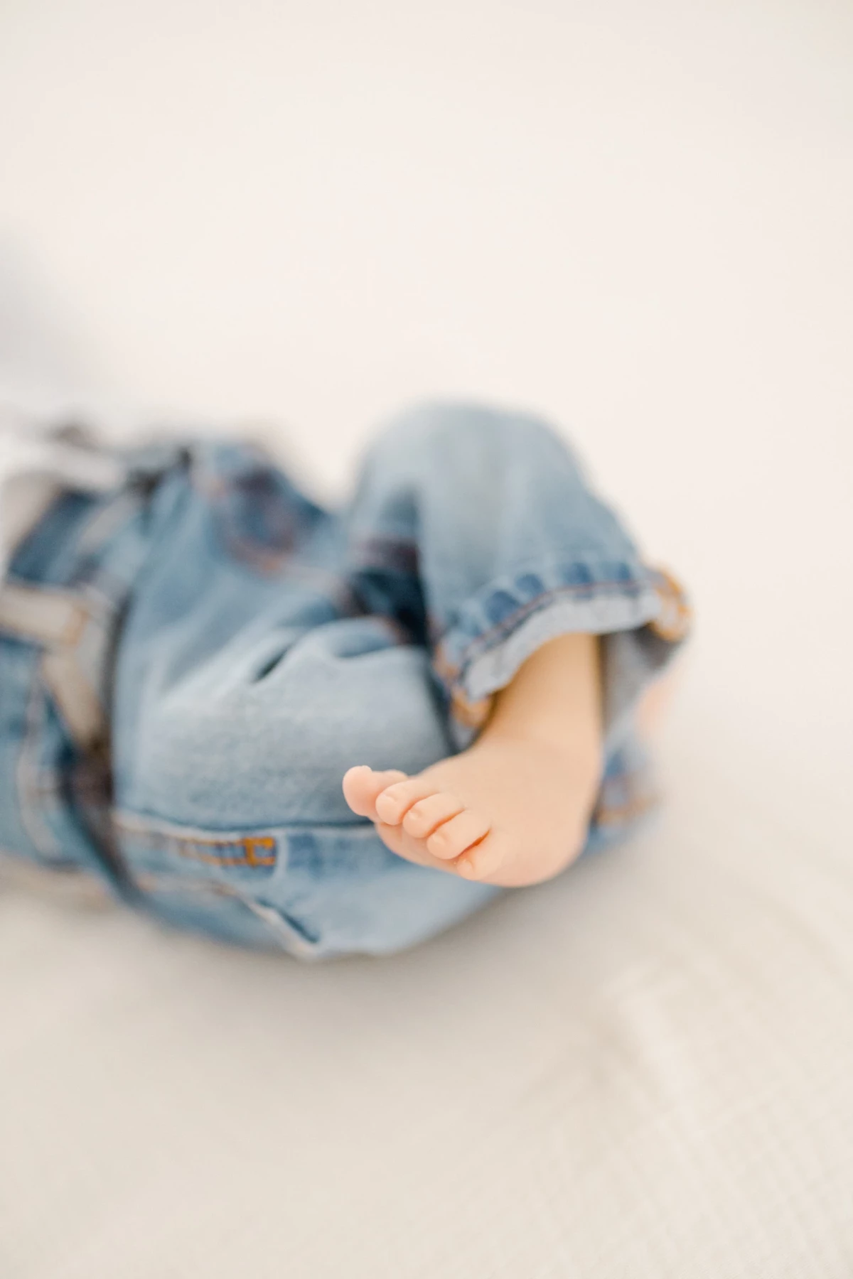 Séance naissance en studio : pieds de bébé dépassant d'un jean, instant tendre et poétique capturé avec douceur en Vendée