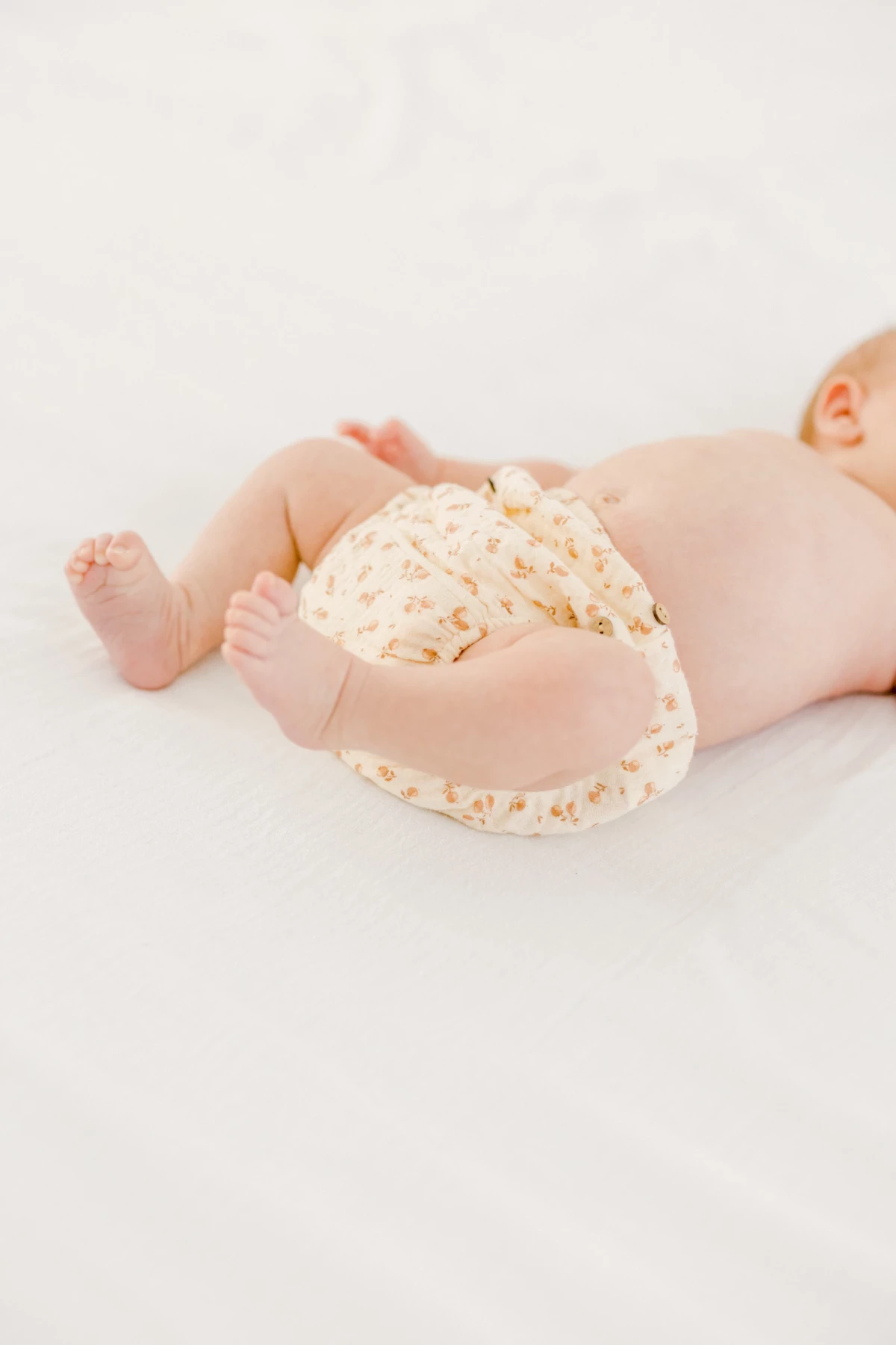 Séance nouveau-né en studio : bébé allongé sur fond blanc, couche fleurie beige, instant de tendresse et douceur infinie