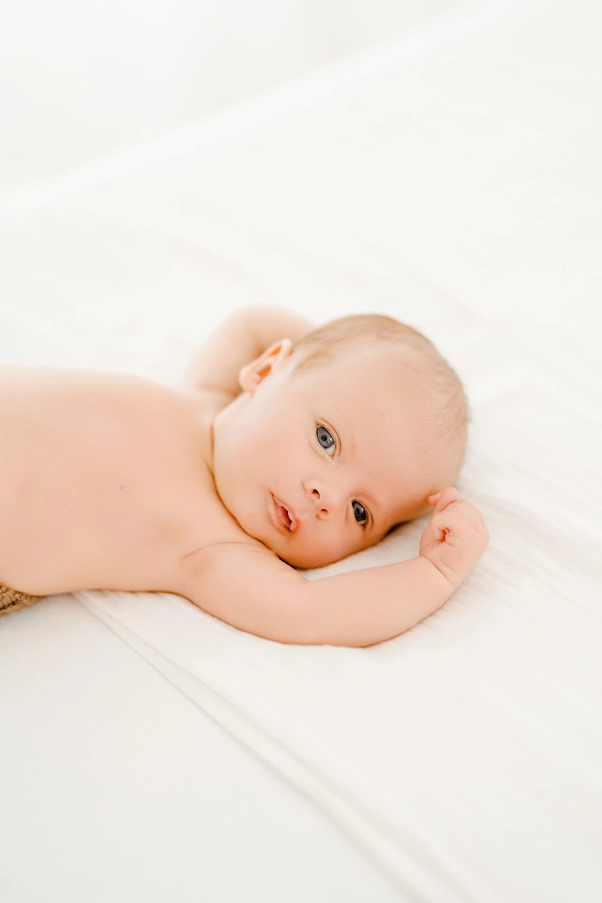 Séance nouveau-né en studio : bébé aux yeux clairs allongé dans une lumière douce et naturelle, tendresse et pureté
