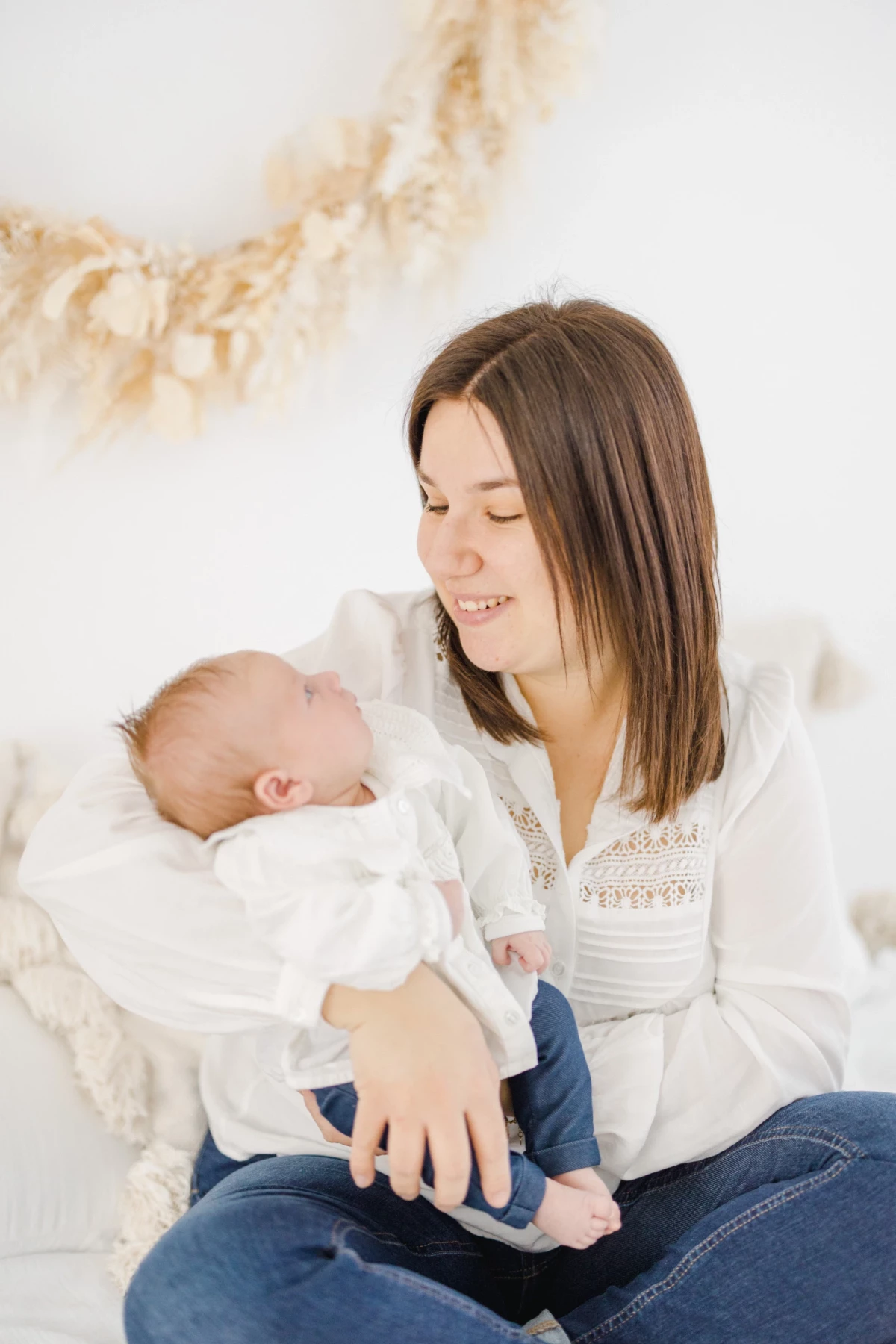 Séance nouveau-né en studio : maman regarde son bébé avec tendresse dans une ambiance douce et lumineuse, tout en blanc