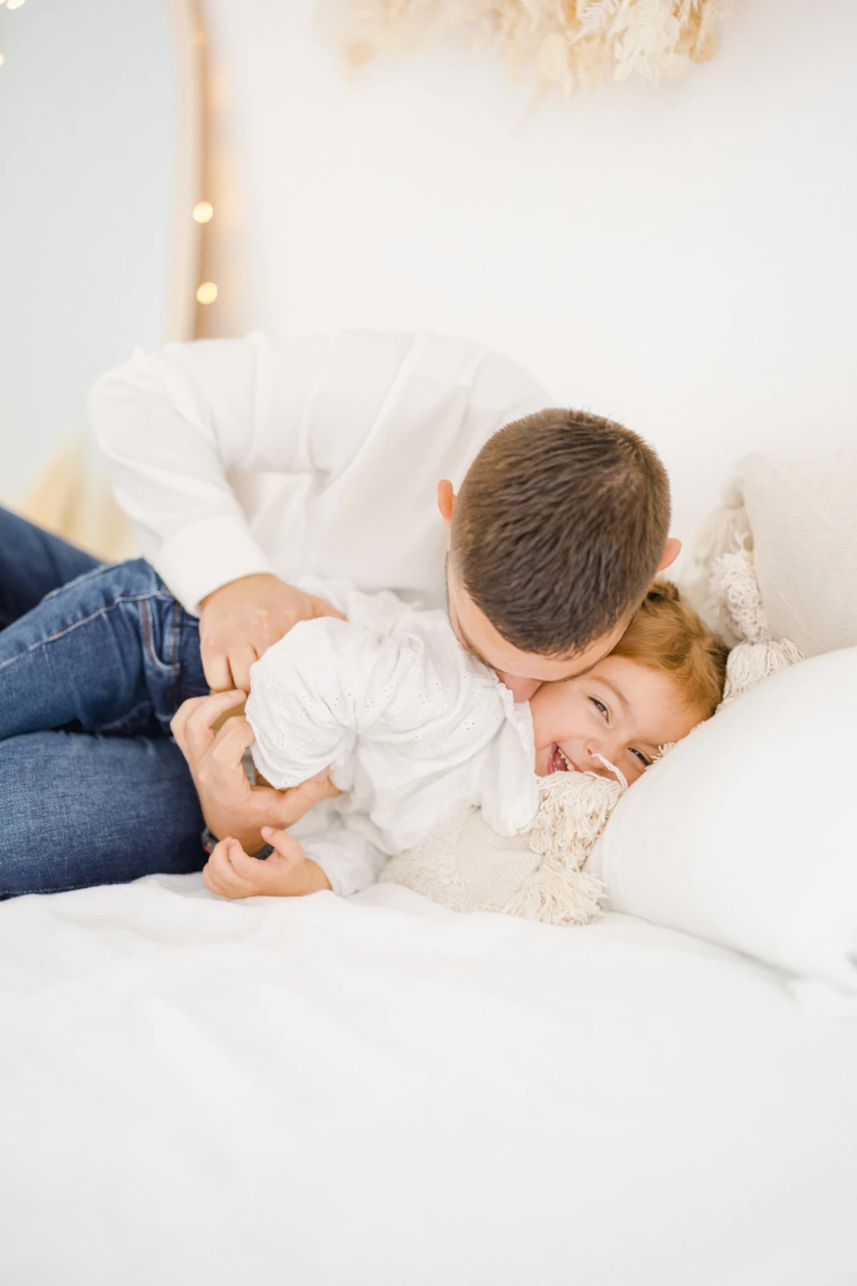 Séance naissance en studio : grand frère enlace tendrement son petit bébé allongé sur un canapé blanc, moment de douceur fraternelle