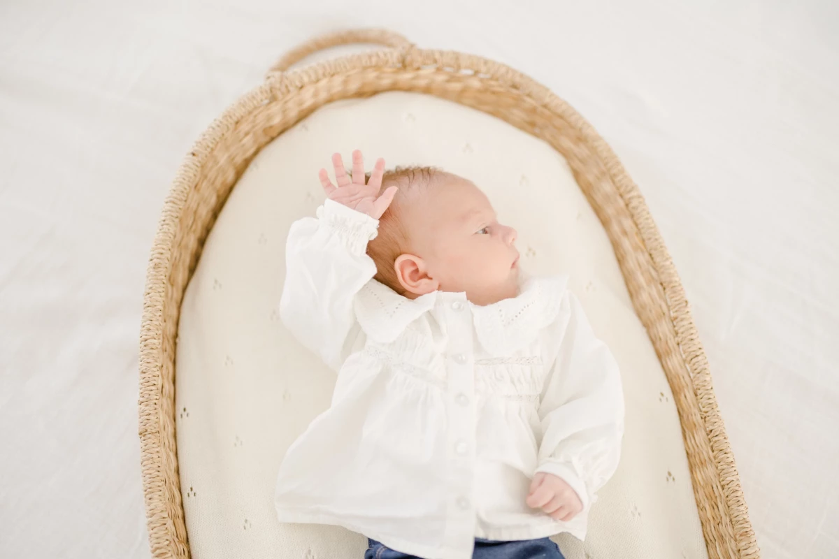 Séance naissance en studio : bébé paisible dans un couffin beige, vêtu de blanc, instant de tendresse capturé en lumière douce