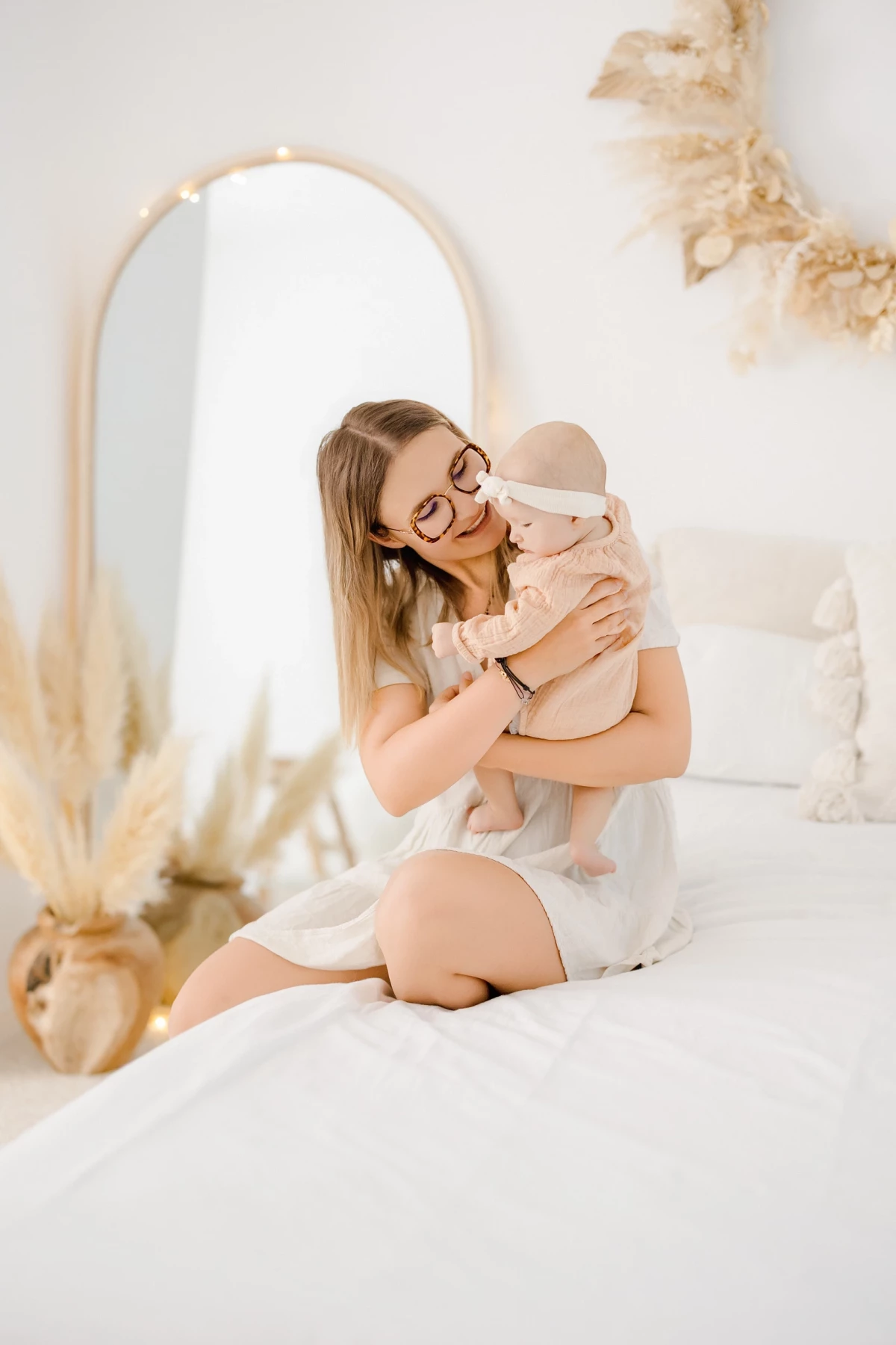 Séance naissance en studio : jeune maman câline son bébé de 4 mois dans une ambiance douce et lumineuse, décor beige et blanc.