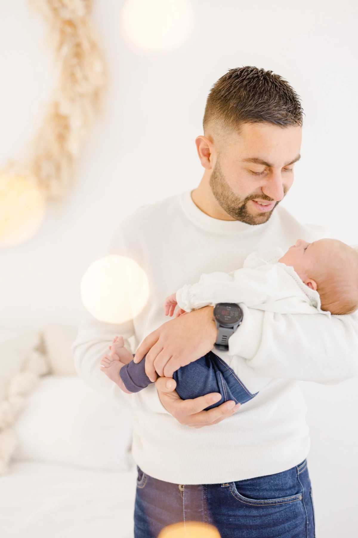 Séance naissance en studio : jeune papa tient son nouveau-né contre lui avec tendresse dans une ambiance douce et lumineuse