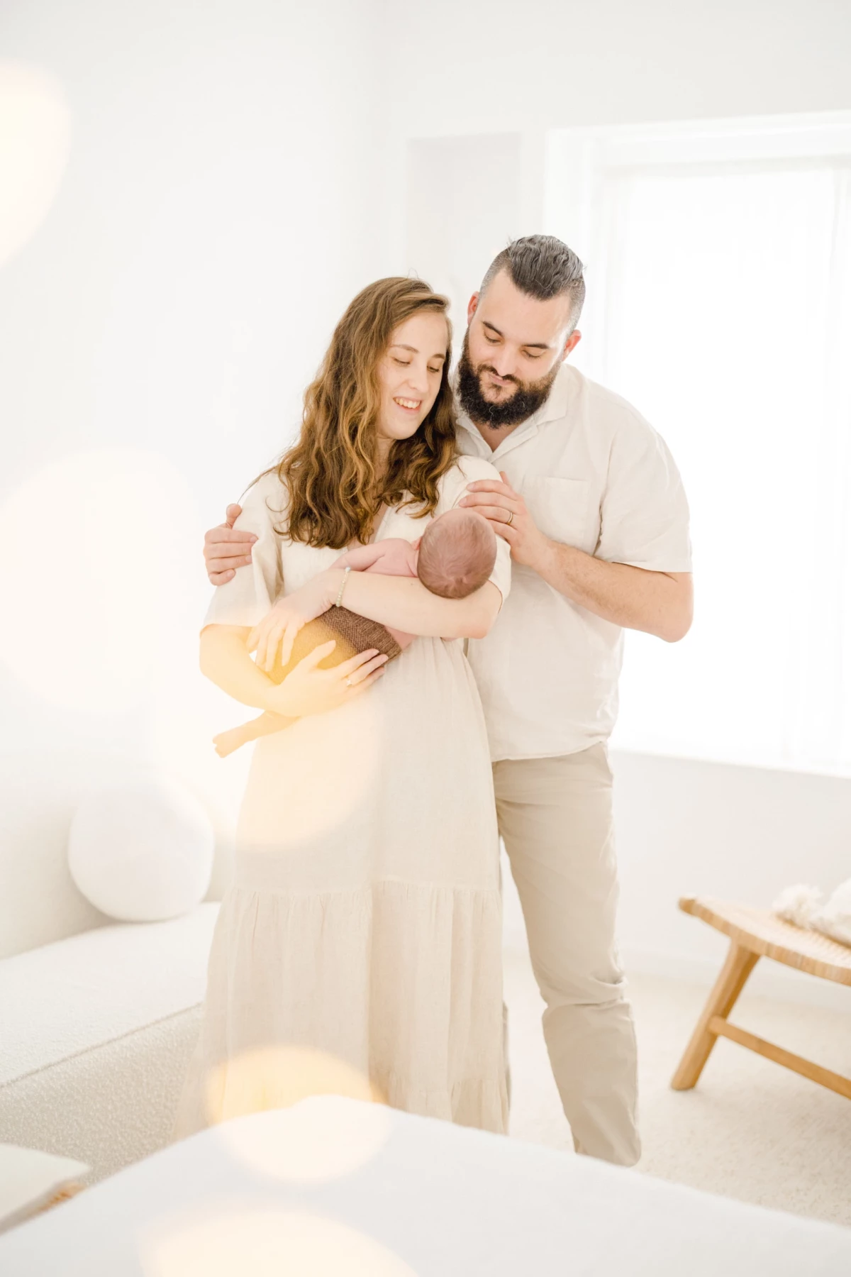 Séance nouveau-né en studio : jeunes parents enlacent leur bébé dans une lumière douce, tendresse et complicité familiale en tons beiges