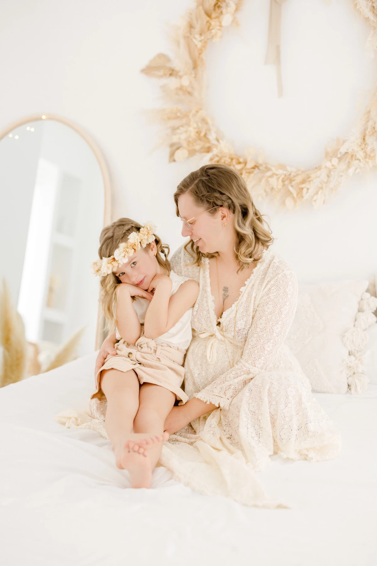 Séance grossesse en famille au studio : maman et petite fille partagent un moment de tendresse sur fond blanc, fleurs séchées