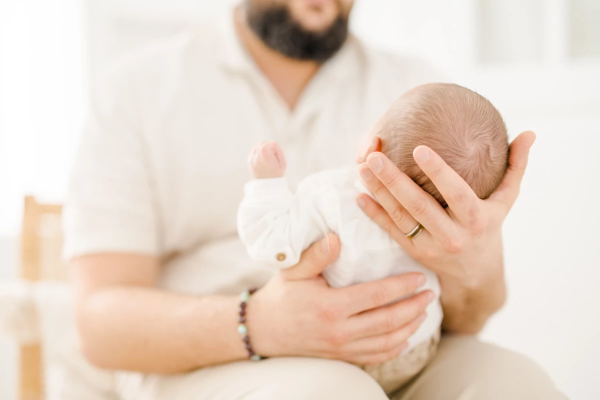 Séance naissance en studio : papa tient délicatement son nouveau-né dans ses bras, instant de tendresse et douceur paternelle