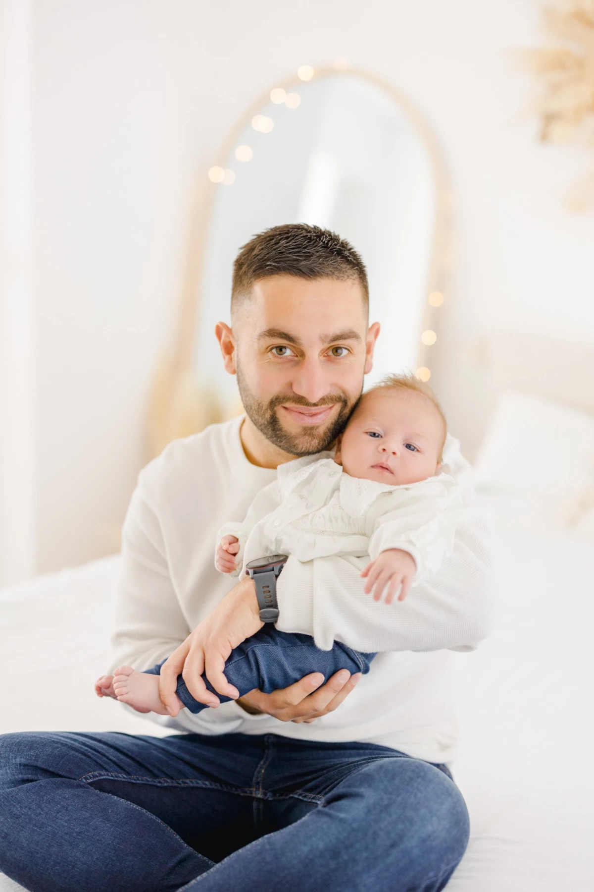 Séance naissance en studio : jeune papa sourit en tenant son nouveau-né dans ses bras, moment de tendresse et de douceur