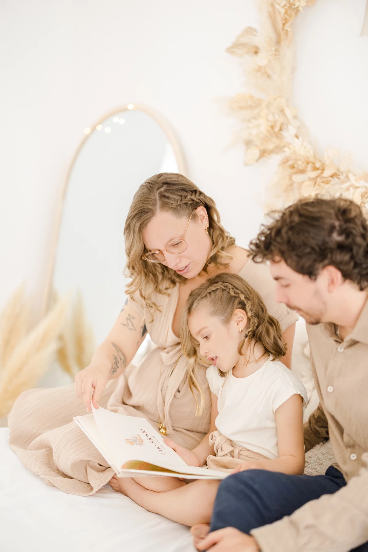 Séance famille en studio : parents et fillette lisent ensemble un livre, partageant un moment de tendresse et complicité dans une ambiance douce
