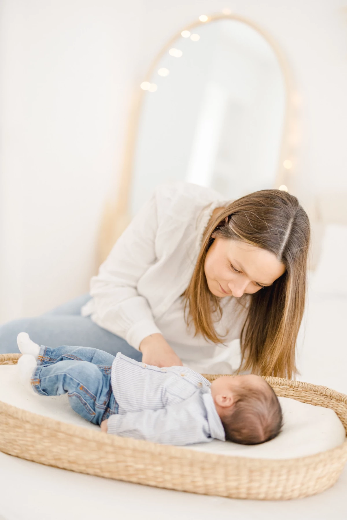 Séance naissance en studio : maman regarde tendrement son nouveau-né dans un panier, instant de douceur et connexion naturelle
