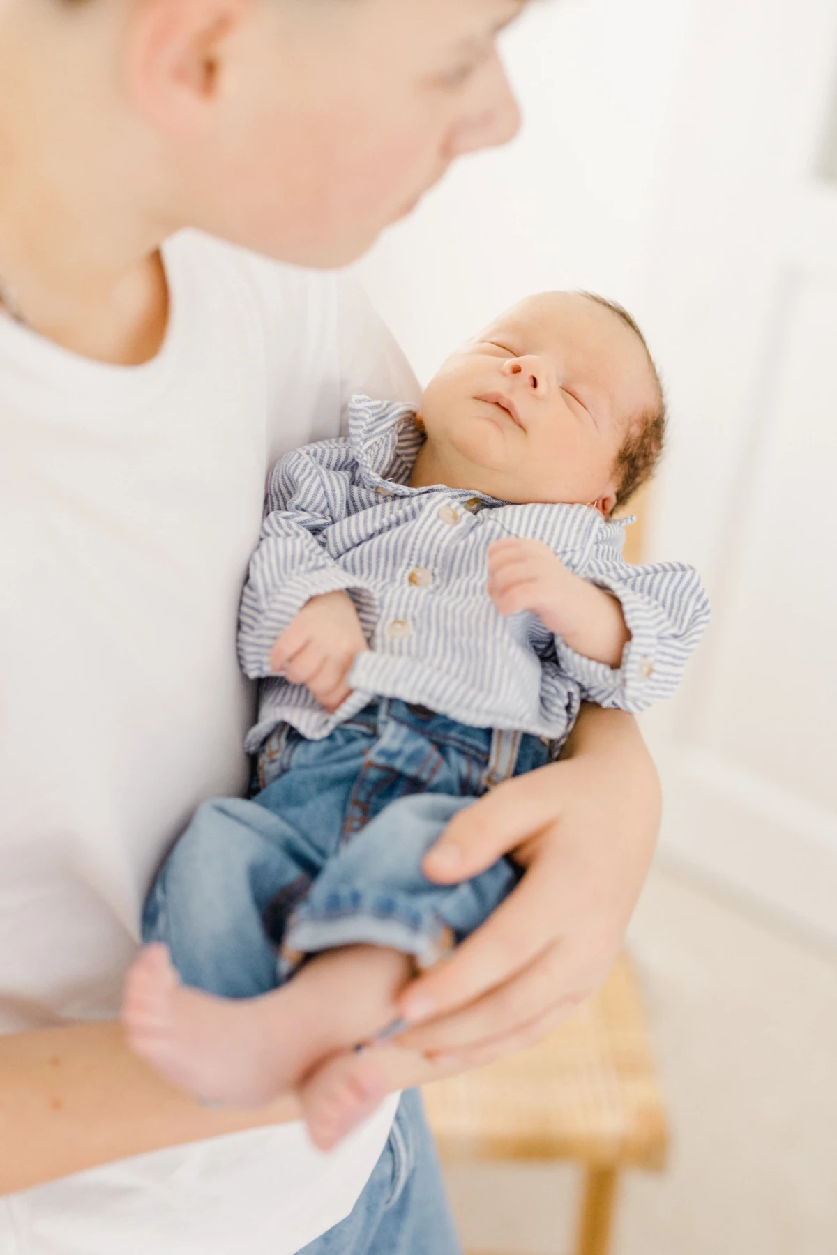 Séance naissance en studio : parent tient son nouveau-né endormi, moment de douceur et tendresse infinie en lumière naturelle
