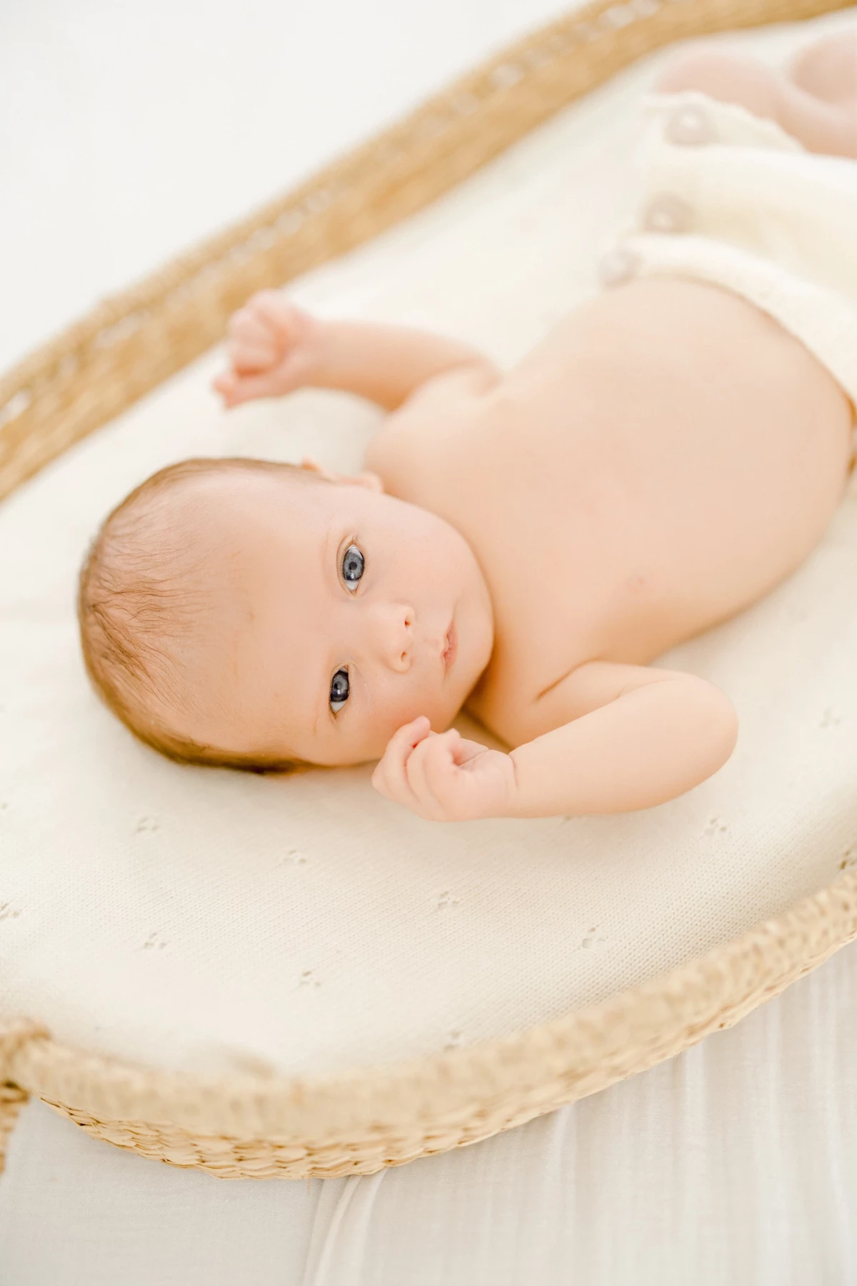 Séance nouveau-né en studio : bébé éveillé allongé sur textile blanc, regard doux et paisible dans une lumière naturelle