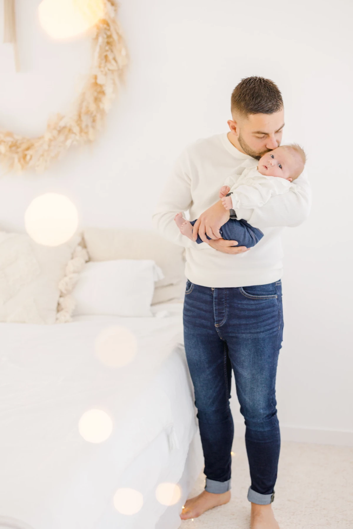 Séance naissance en studio : jeune papa embrasse tendrement son nouveau-né dans une ambiance lumineuse et épurée