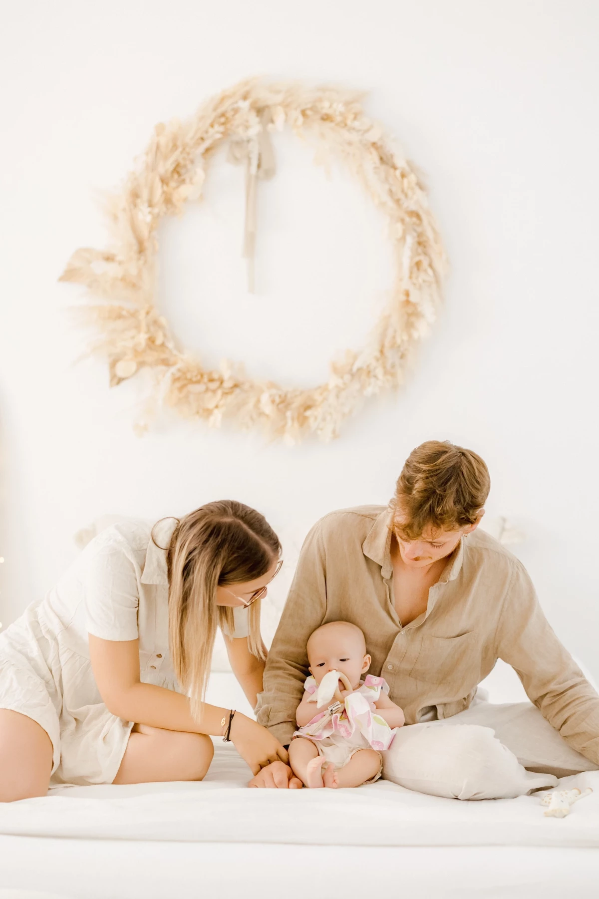 Séance naissance en studio : parents enlacent leur bébé de 4 mois dans une ambiance douce et lumineuse, tons beige et blanc