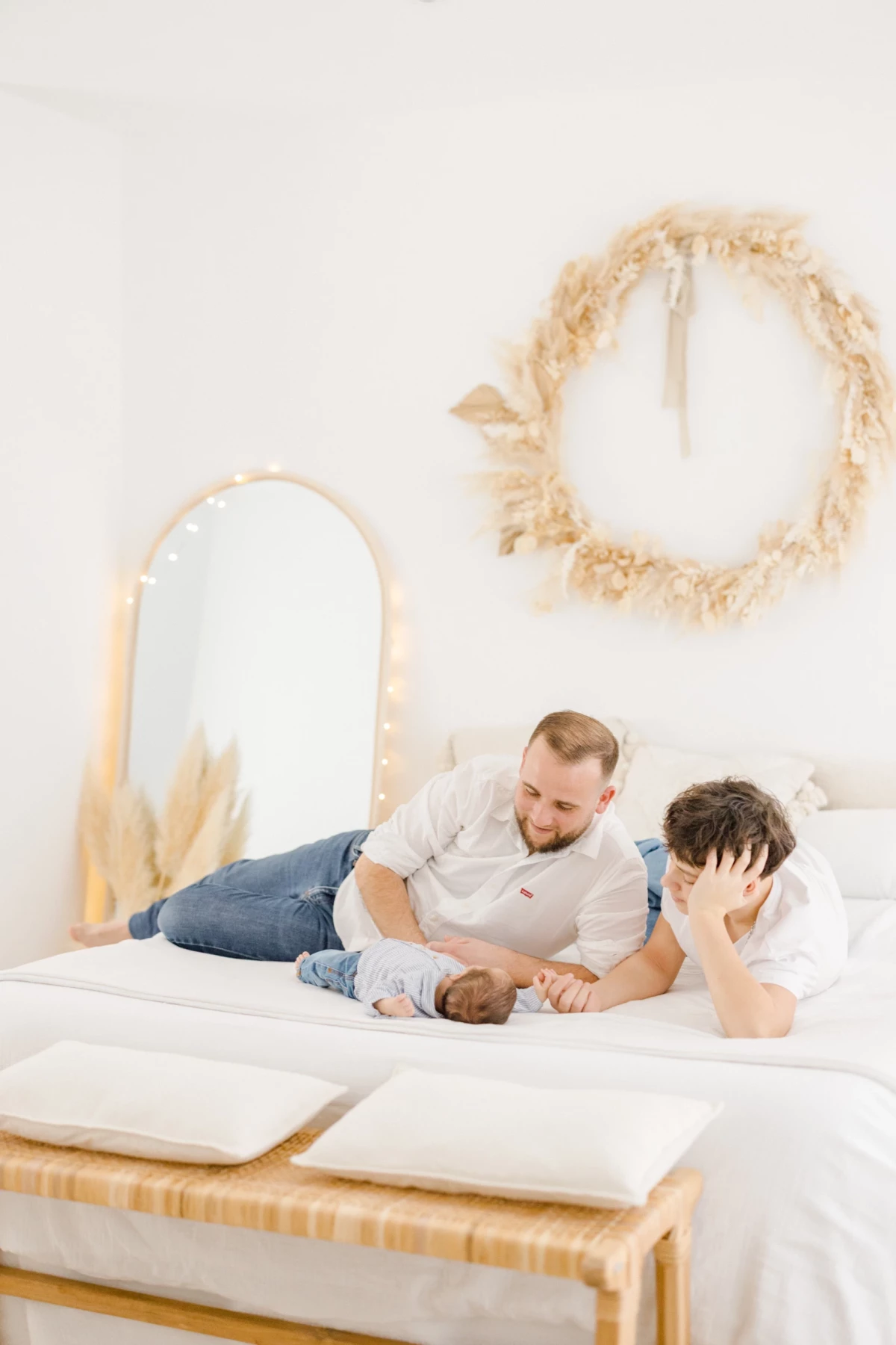 Séance naissance en studio : père et grand frère contemplent avec tendresse le nouveau-né allongé sur un lit blanc épuré