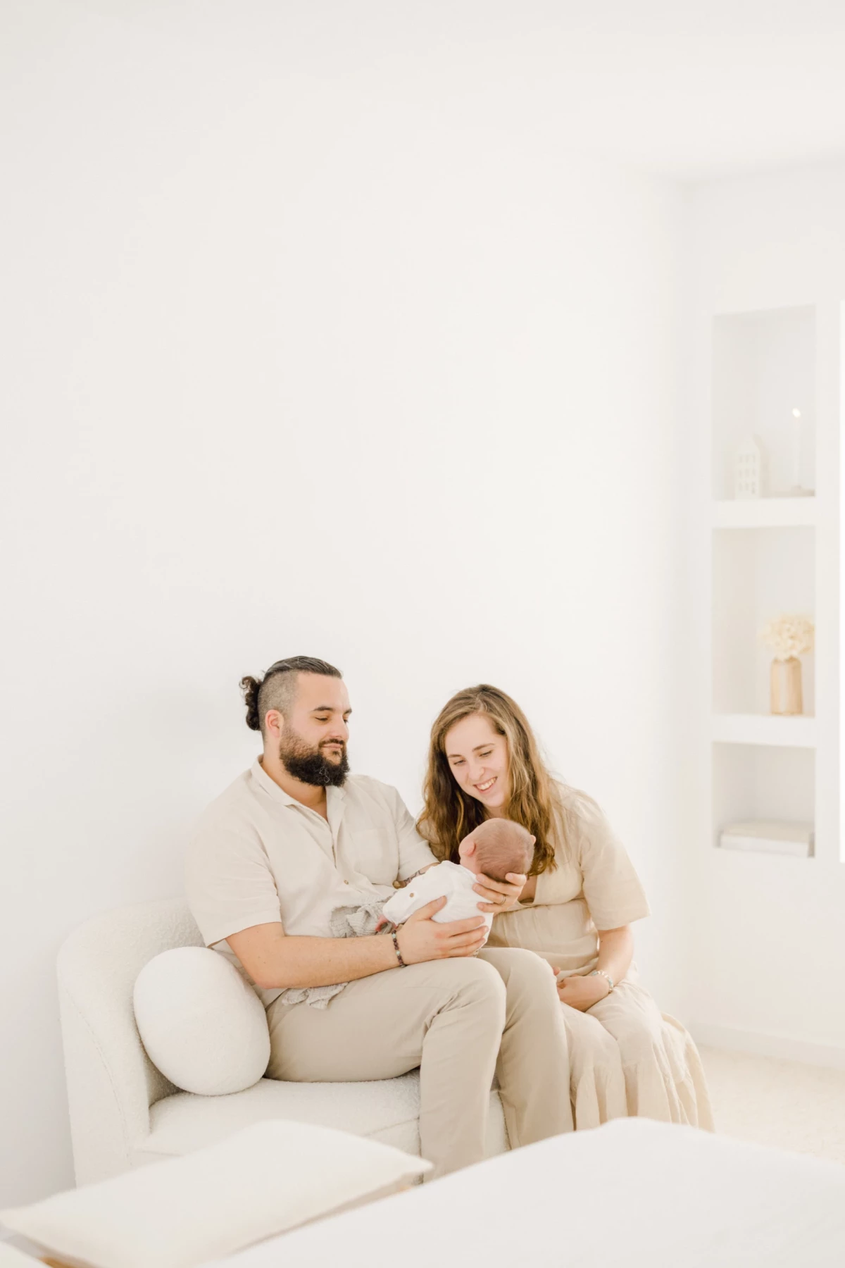 Séance naissance en studio : jeune couple contemple leur nouveau-né avec tendresse dans une atmosphère de douceur immaculée
