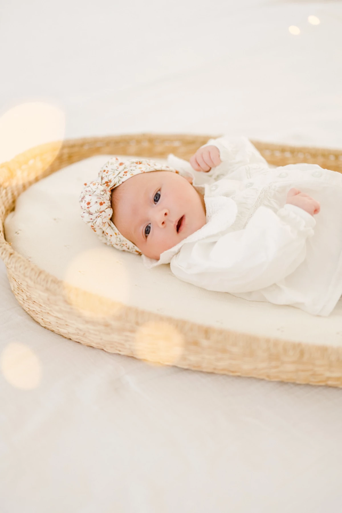 Séance nouveau-né au studio : bébé éveillé repose dans un couffin en osier, regard tendre et paisible dans une ambiance naturelle