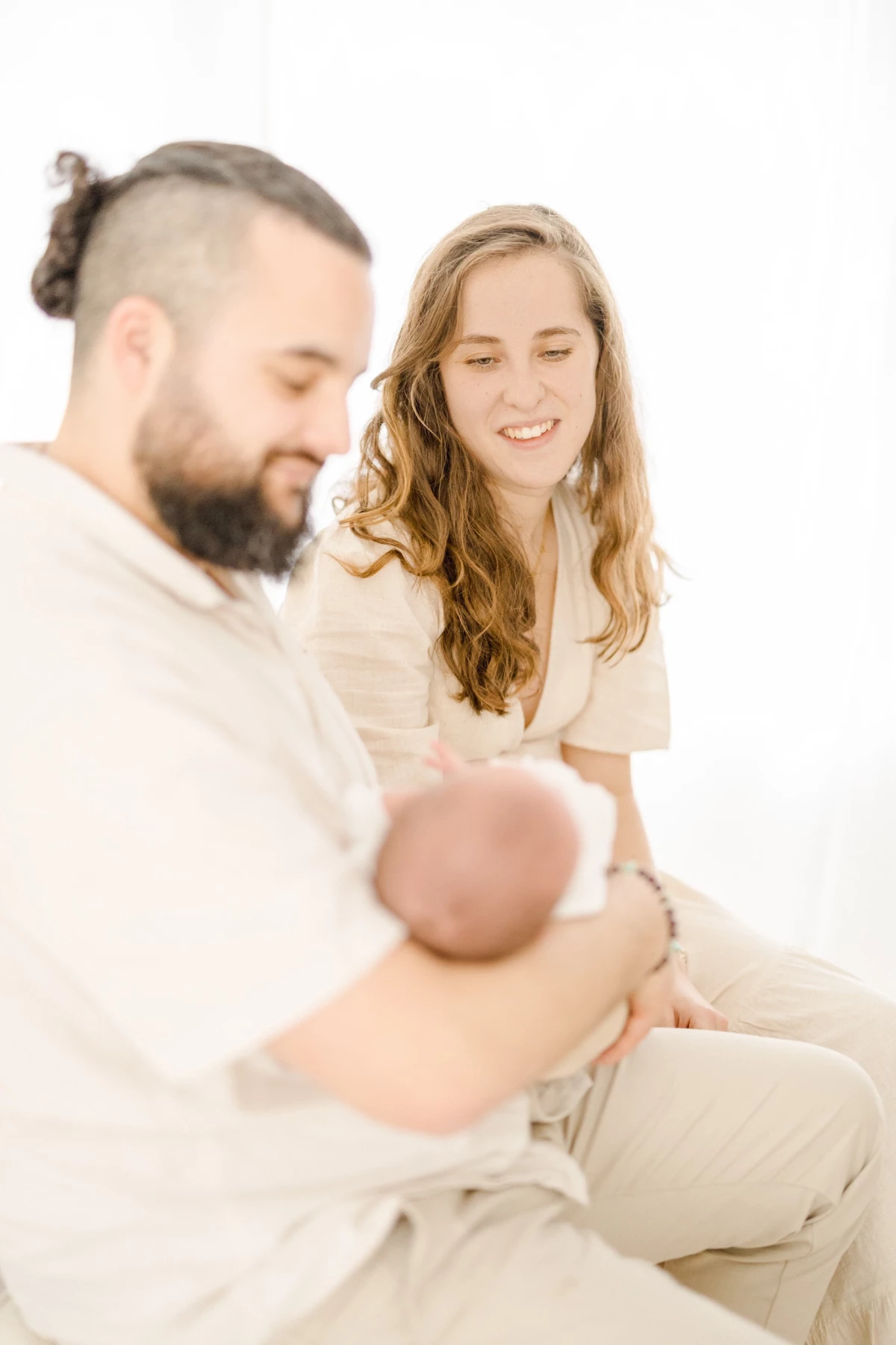 Séance naissance en studio : parents admirent leur nouveau-né avec tendresse dans une ambiance de douceur lumineuse
