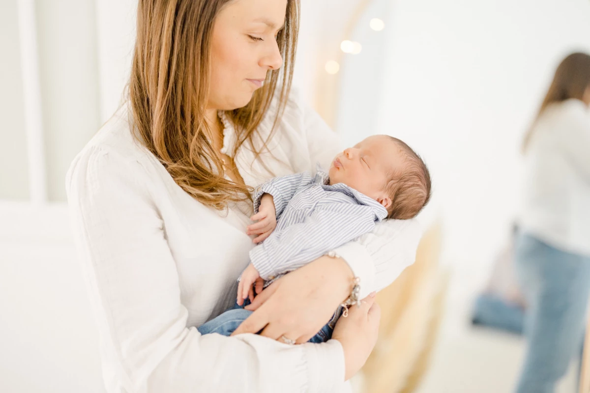 Séance naissance en studio : jeune maman berce son nouveau-né dans ses bras, instant de douceur et d'amour maternel intemporel