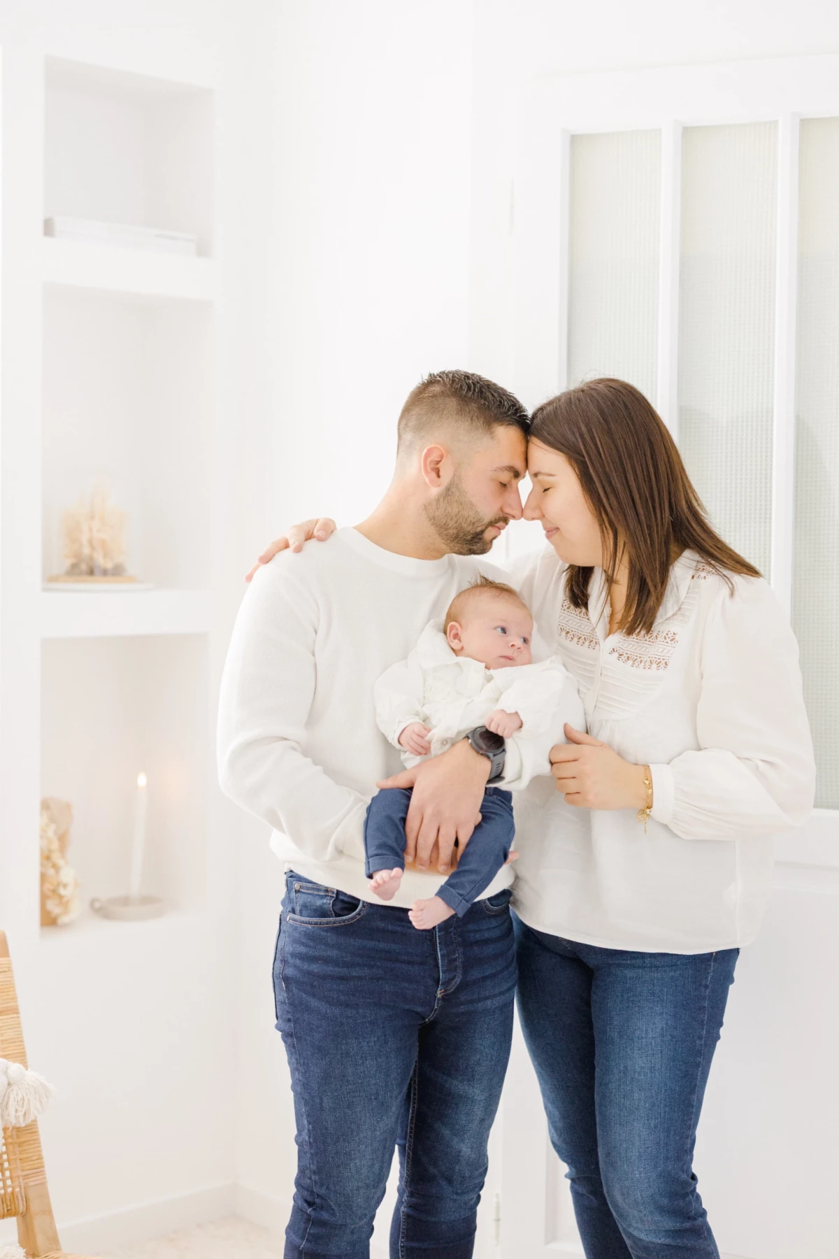 Séance naissance en studio : jeunes parents enlacés avec leur nouveau-né, ambiance douce et intemporelle sur fond blanc immaculé