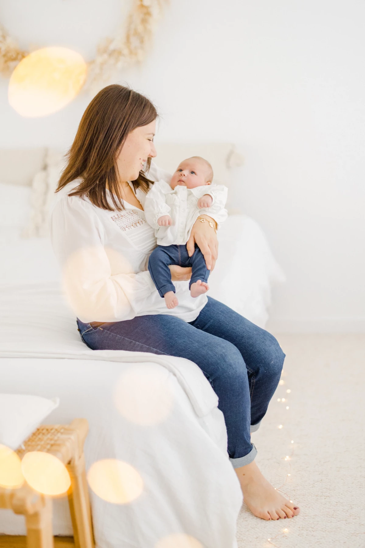 Séance naissance au studio : maman en pull blanc tient son nouveau-né dans les bras, lumière douce et décor épuré en Vendée