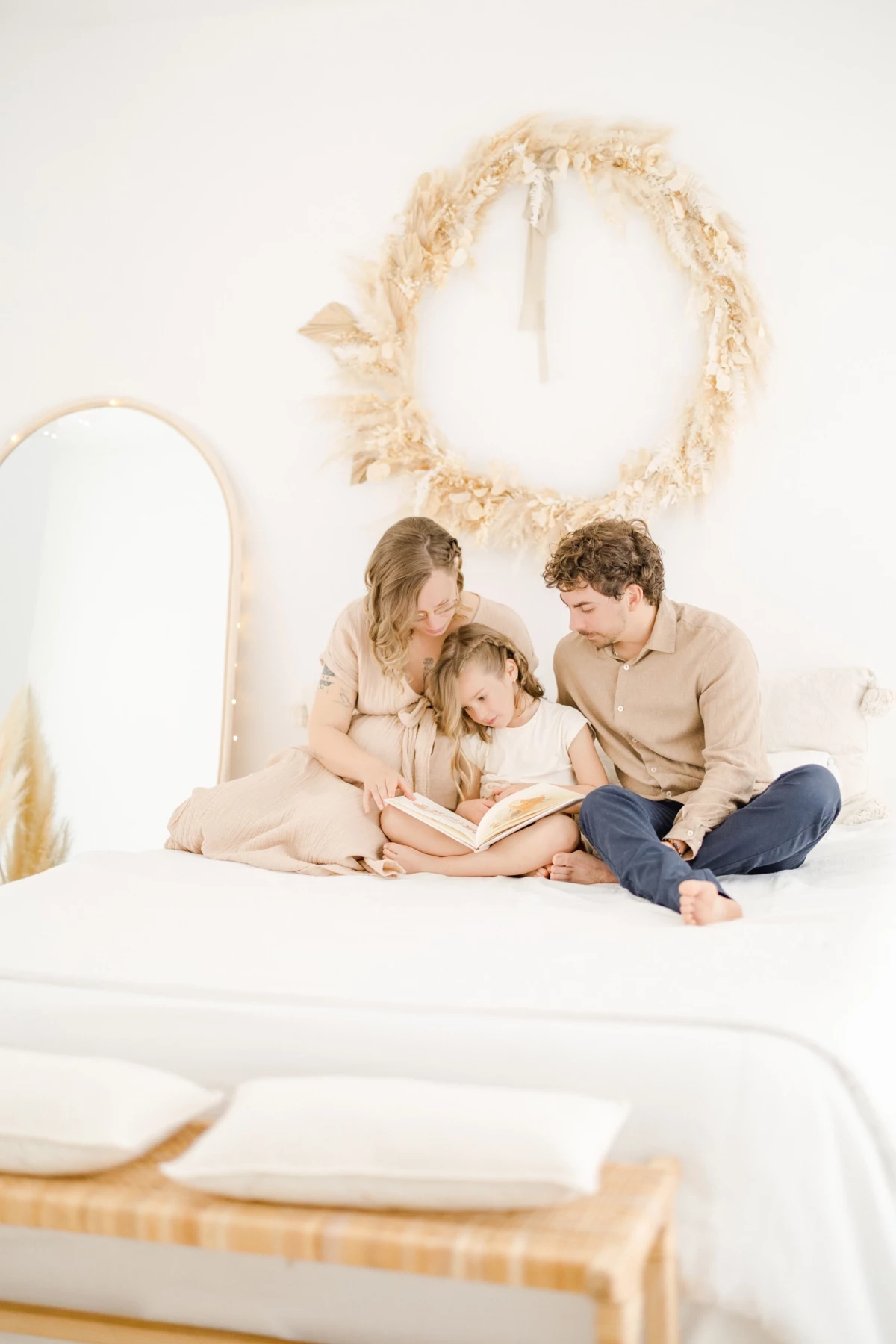 Séance grossesse en famille au studio : parents et enfant partagent un moment de lecture complice dans une ambiance douce et épurée