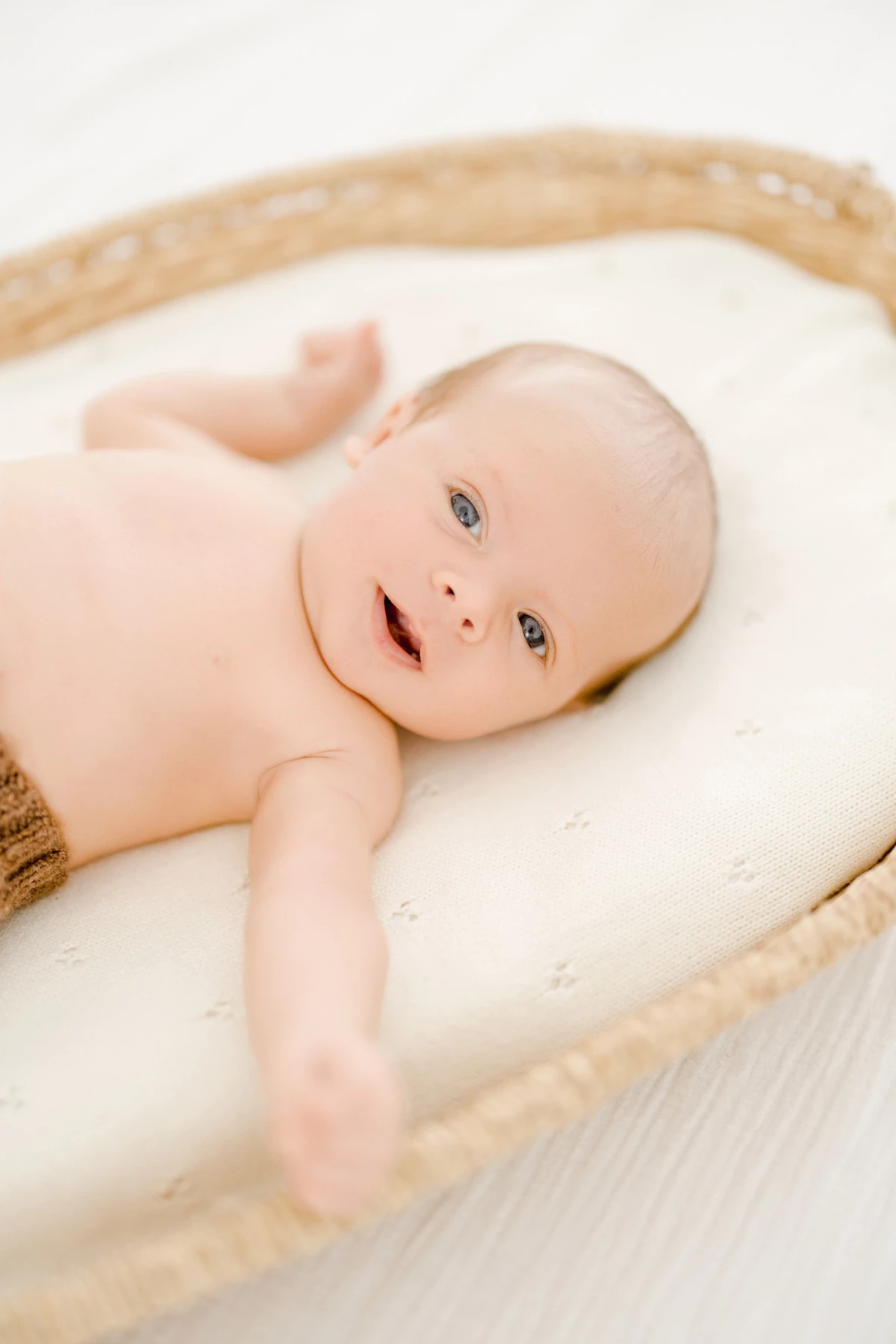 Séance nouveau-né au studio : bébé éveillé repose dans un panier tressé, regard curieux dans une lumière douce et naturelle