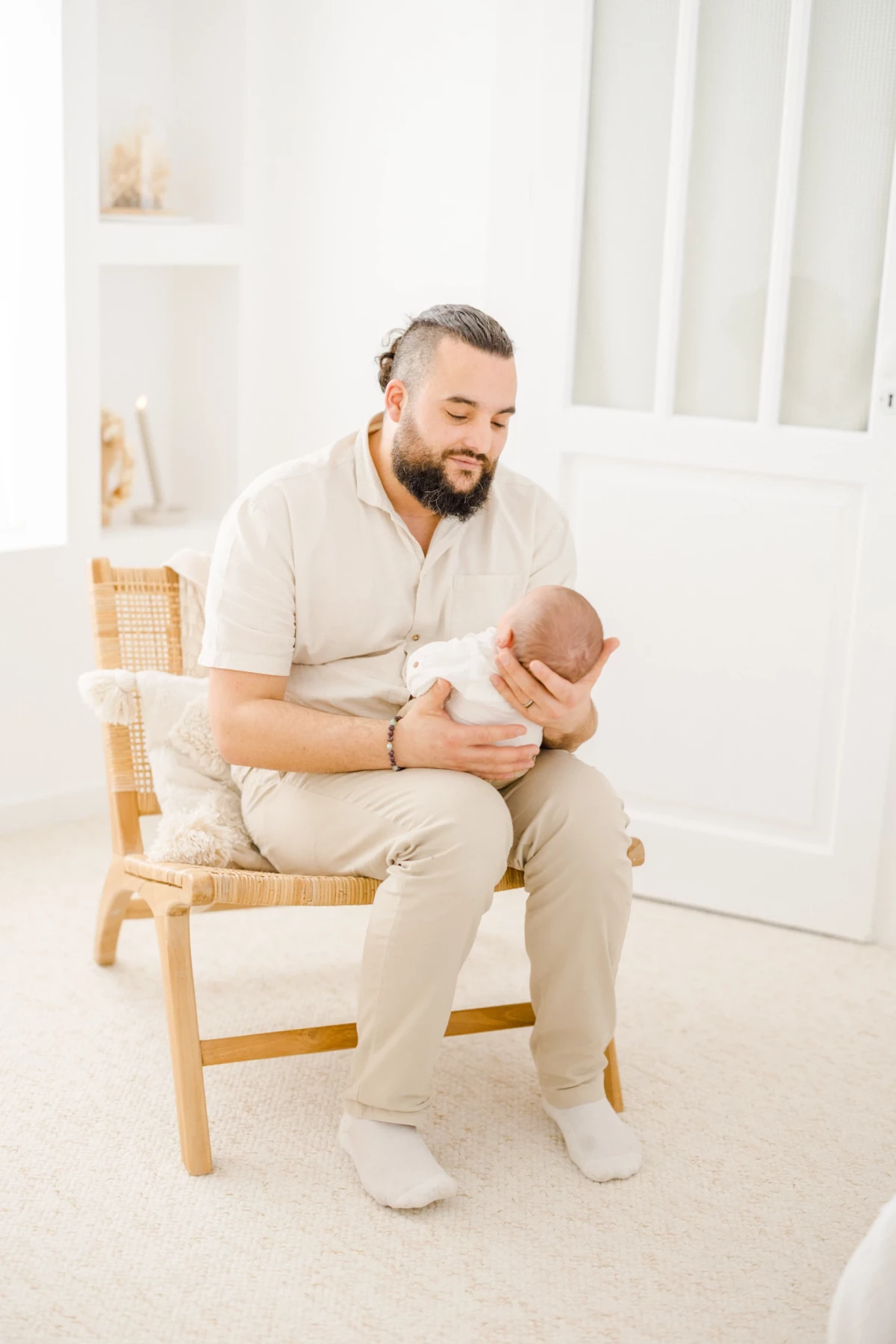 Séance nouveau-né en studio : jeune papa berce tendrement son bébé dans ses bras, lumière douce et intemporelle, Vendée