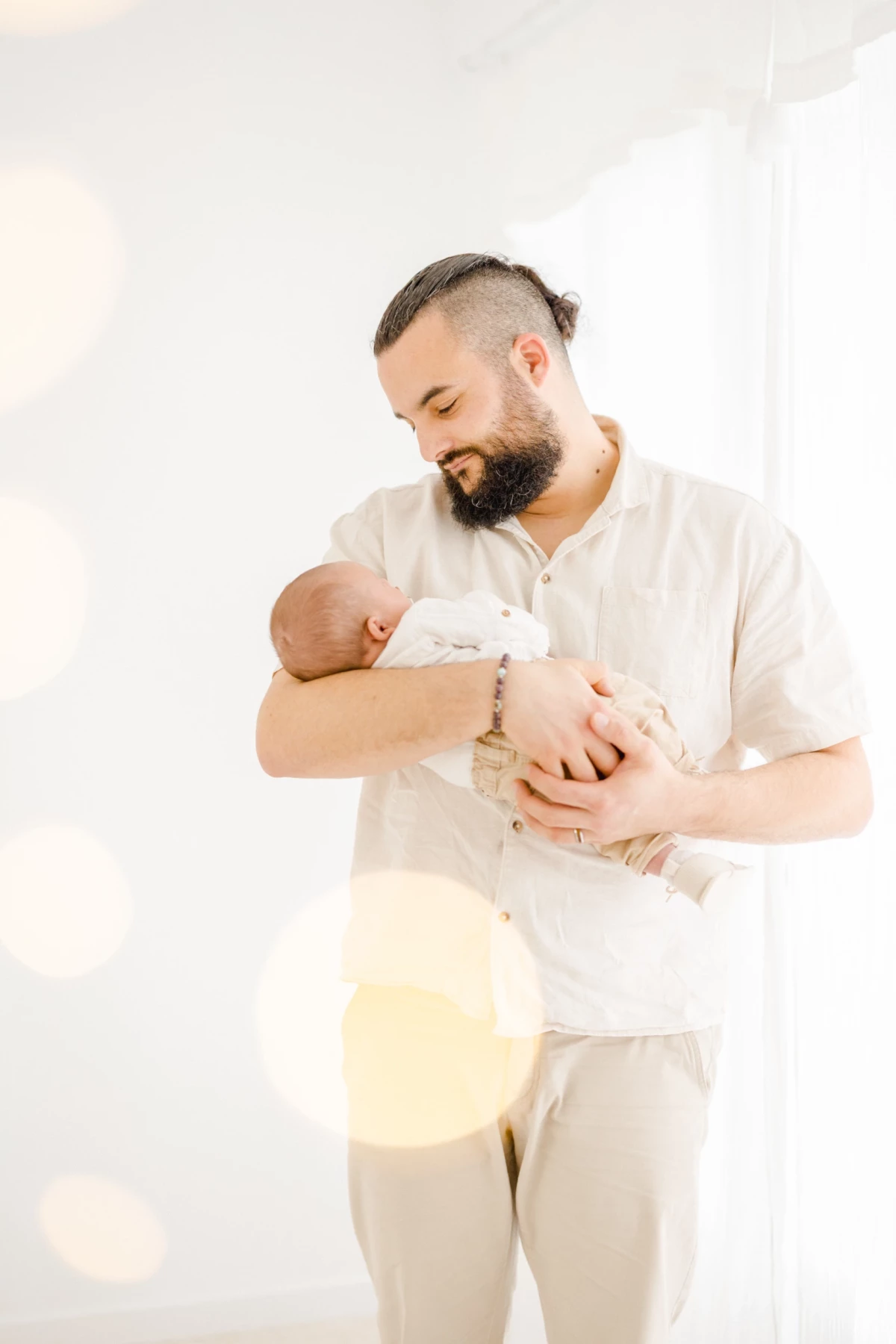 Séance nouveau-né en studio : papa berce son bébé avec tendresse dans une lumière douce et naturelle, instant de bonheur familial