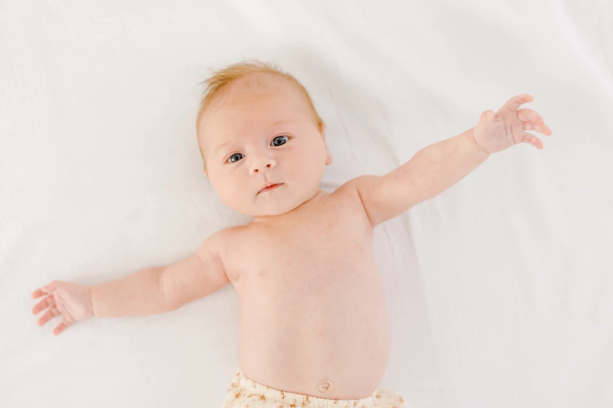 Séance nouveau-né en studio : bébé allongé sur fond blanc, bras ouverts dans un geste de douceur et de sérénité