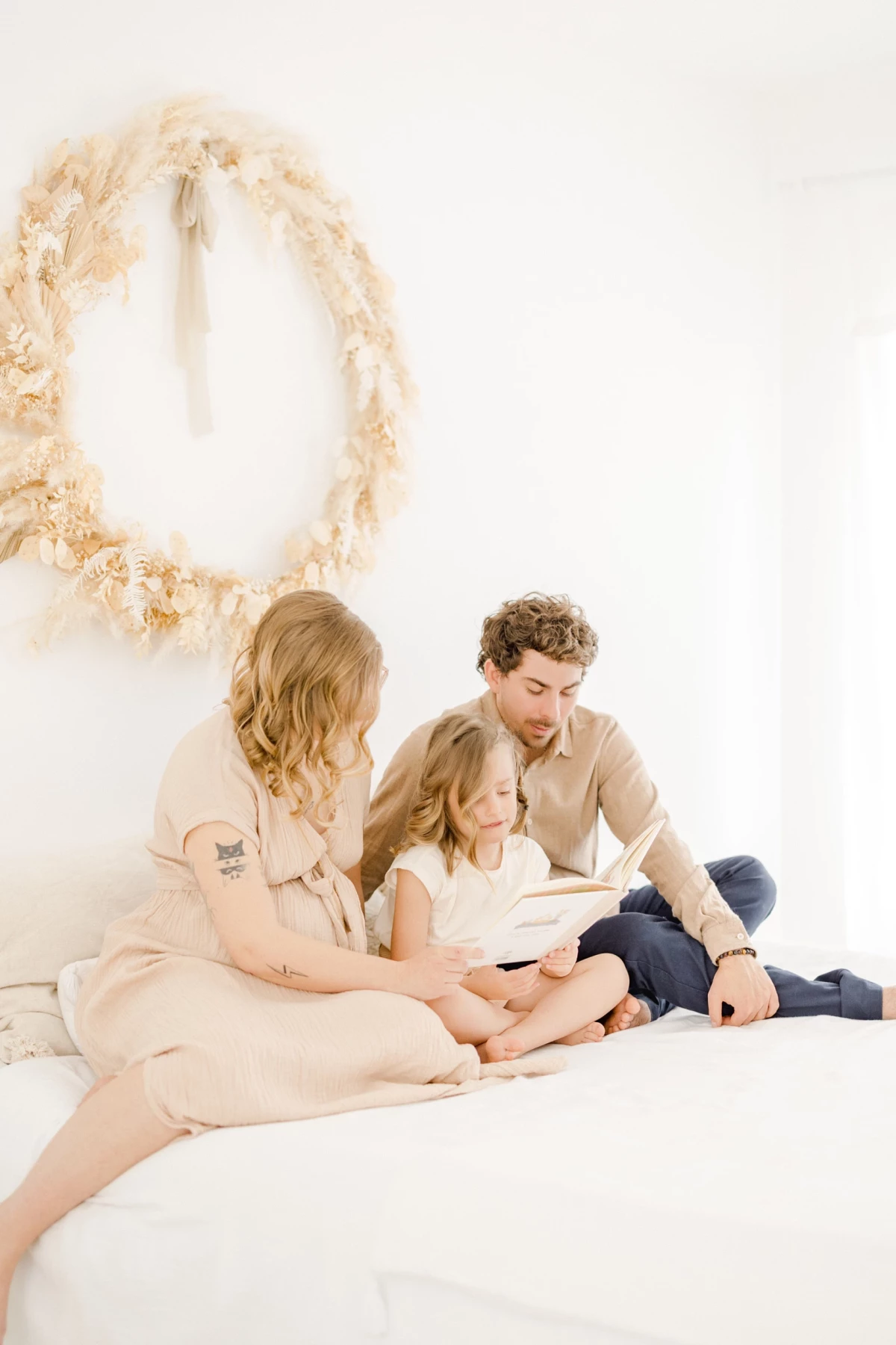 Séance grossesse en famille au studio : parents et enfant partagent un moment de lecture dans une ambiance douce et lumineuse