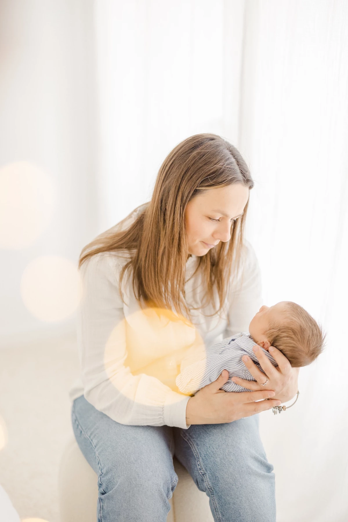 Séance naissance en studio : jeune maman allaite son nouveau-né dans une ambiance de douceur et d'intimité, tons beige et blanc