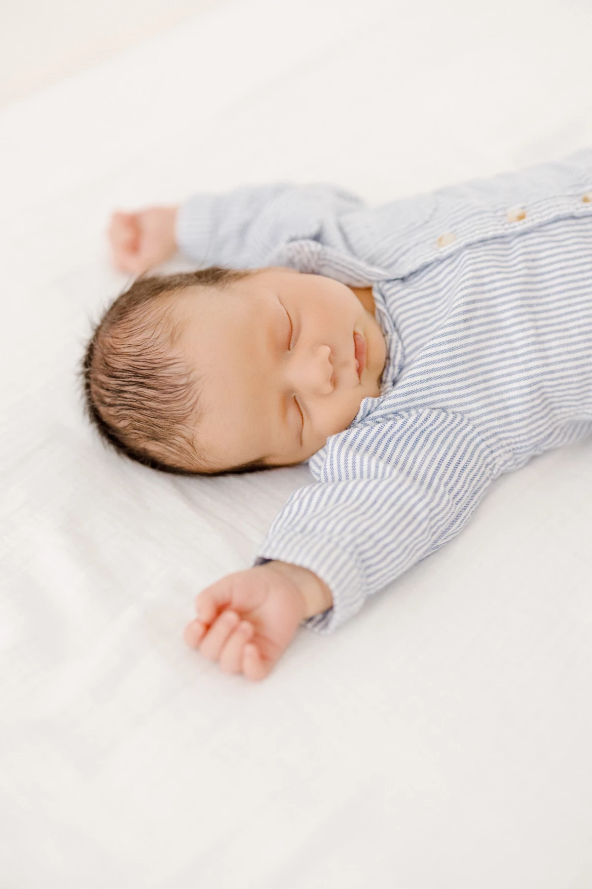 Séance naissance en studio : nouveau-né endormi paisiblement en pyjama rayé, douceur et sérénité des premiers jours