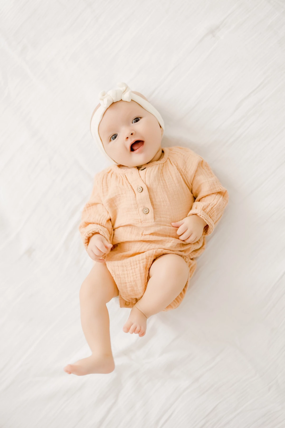 Séance naissance en studio : bébé de 4 mois dans une tenue beige douce, regard éveillé et sourire tendre sur fond blanc lumineux