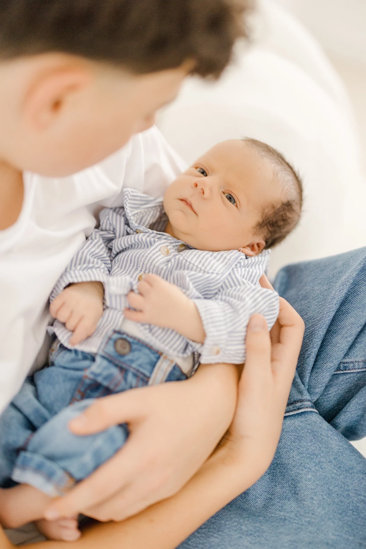 Séance naissance en studio : grand frère contemple son petit frère nouveau-né avec tendresse et émerveillement