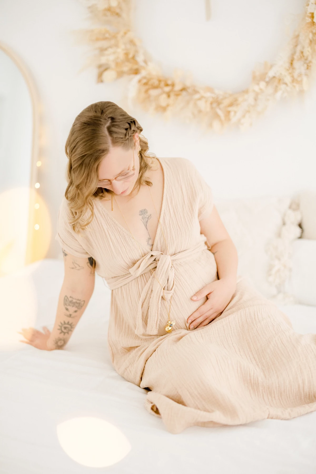 Séance grossesse au studio : future maman en robe beige caresse son ventre dans une atmosphère de douceur et de sérénité lumineuse