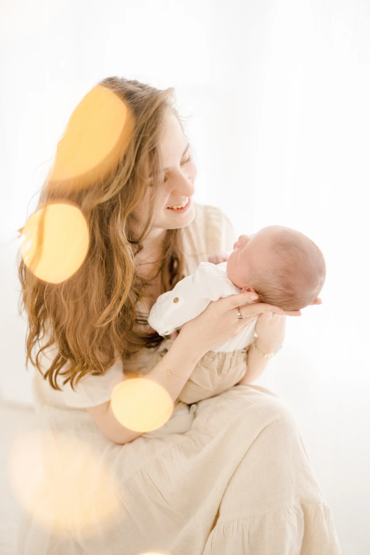 Séance naissance en studio : jeune maman souriante berce tendrement son nouveau-né dans une ambiance de douceur lumineuse