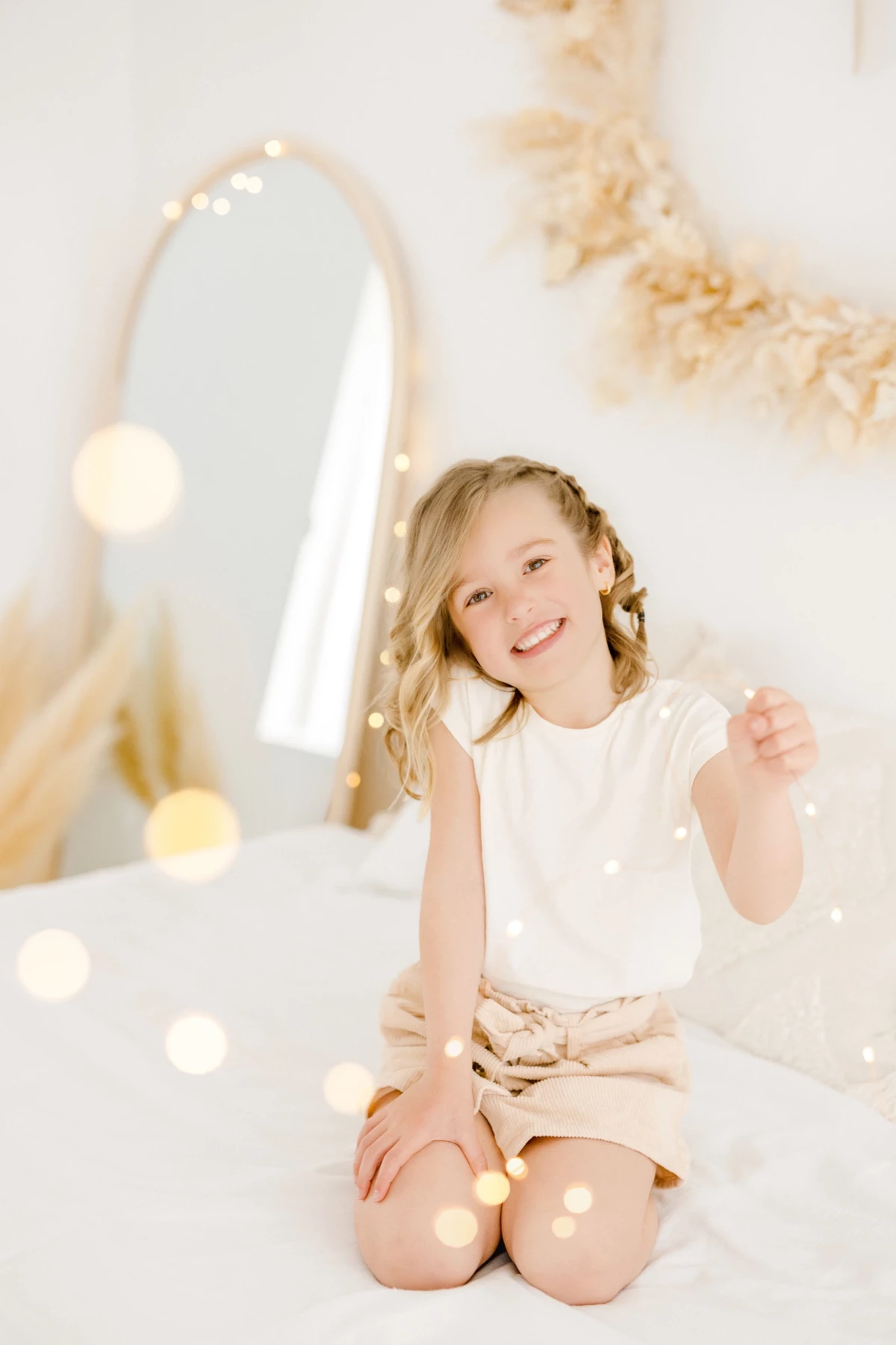 Séance famille en studio : petite fille souriante assise en tailleur dans un décor lumineux et épuré aux tons beige et blanc