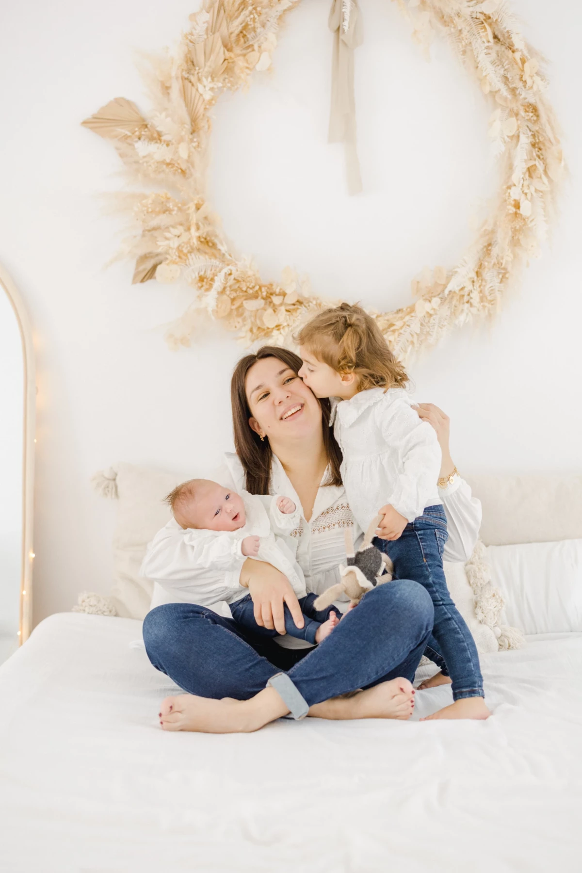 Séance naissance au studio : maman rayonnante avec son nouveau-né et sa fille, tendresse et complicité familiale dans une ambiance lumineuse