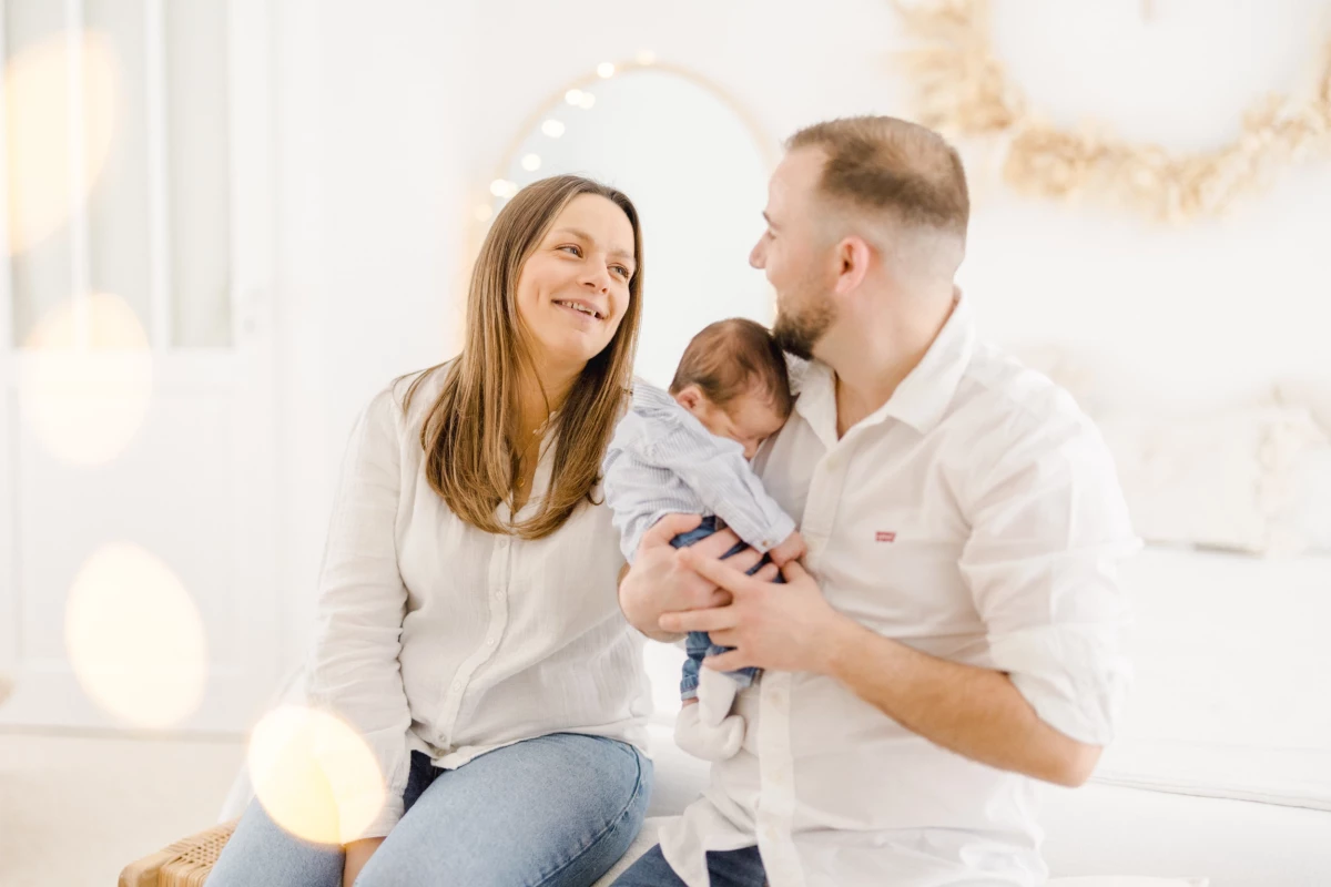 Séance naissance en studio : jeunes parents souriant avec leur nouveau-né, complicité familiale et lumière douce