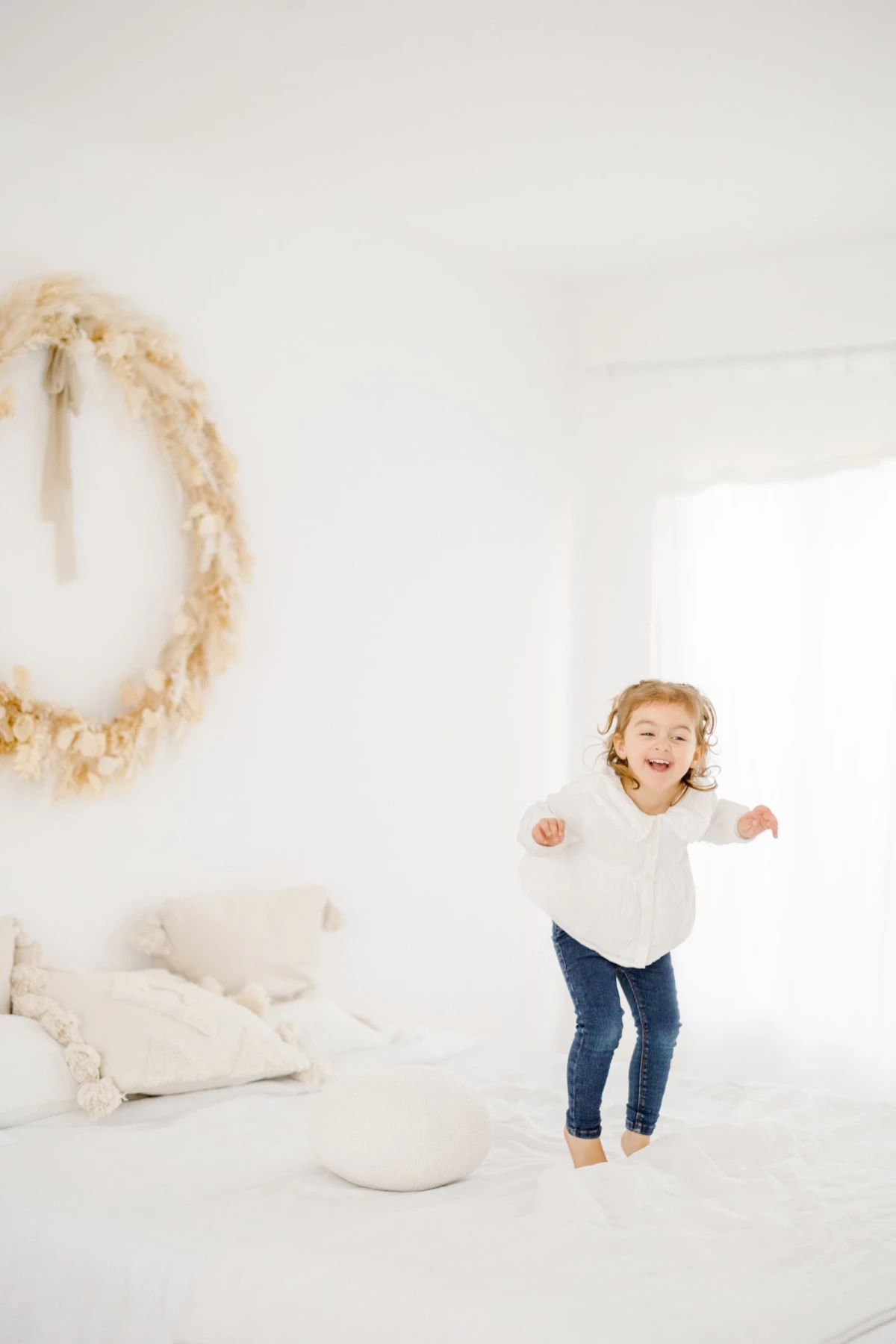 Séance famille en studio : petite fille souriante danse joyeusement dans une ambiance douce et lumineuse aux tons blancs et beiges