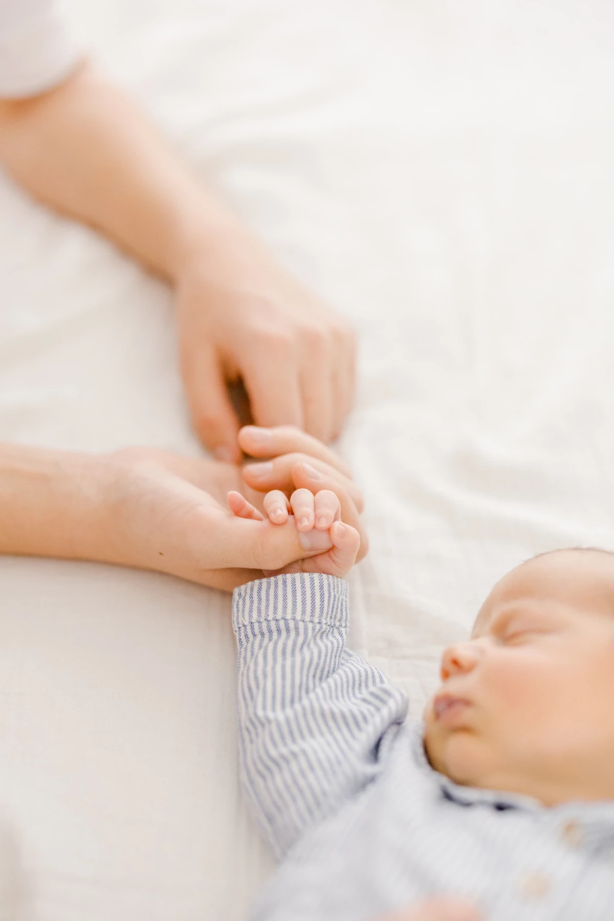 Séance naissance au studio : mains de parents et bébé enlacées dans un geste de tendresse, lumière douce et intimité familiale