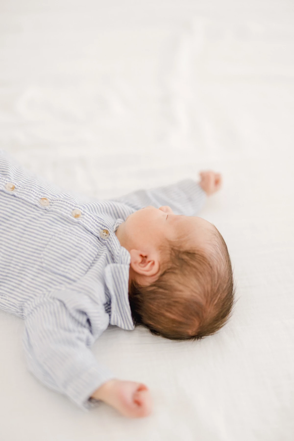Séance naissance en studio : nouveau-né paisible allongé en pyjama rayé sur fond blanc, ambiance douce et intemporelle