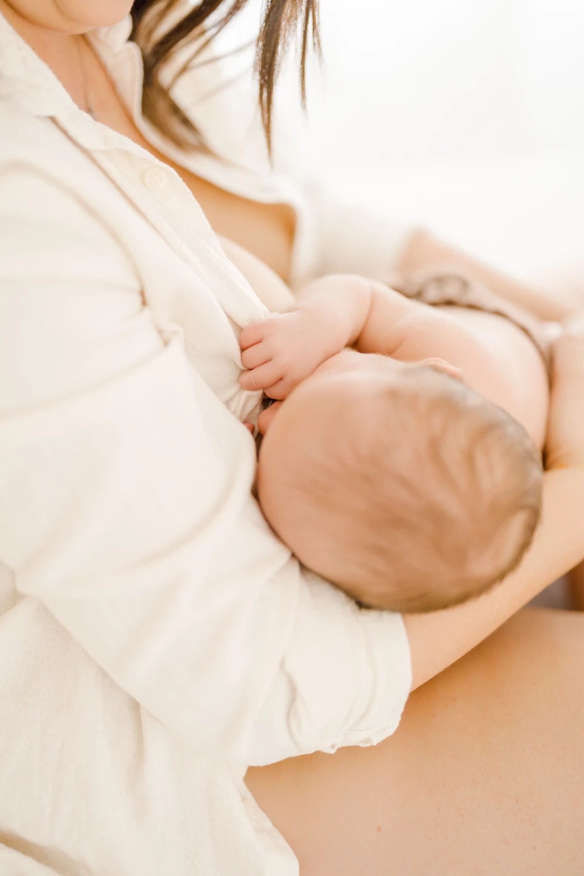 Séance allaitement en studio : maman et nouveau-né en peau à peau dans une lumière naturelle douce, moment d'intimité et de tendresse