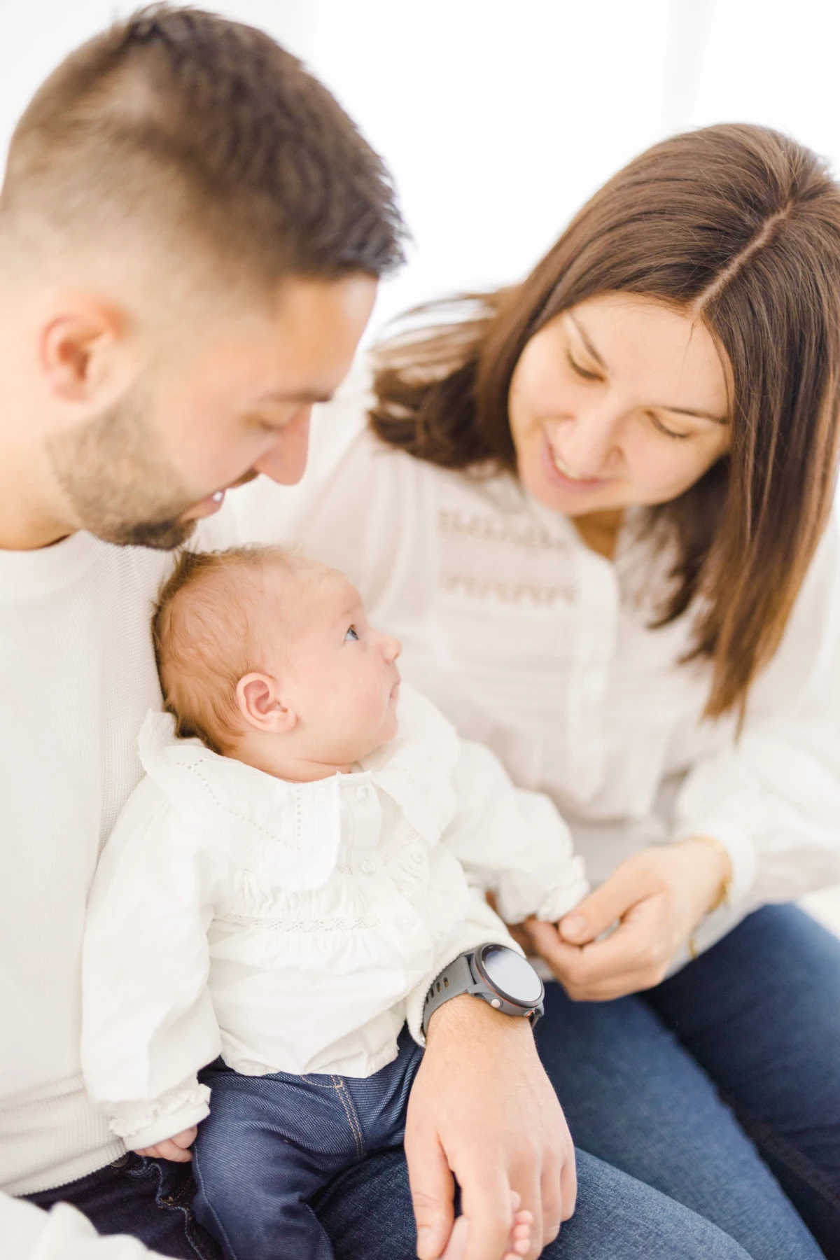 Séance naissance en studio : jeunes parents contemplent leur bébé avec tendresse dans une lumière douce et naturelle