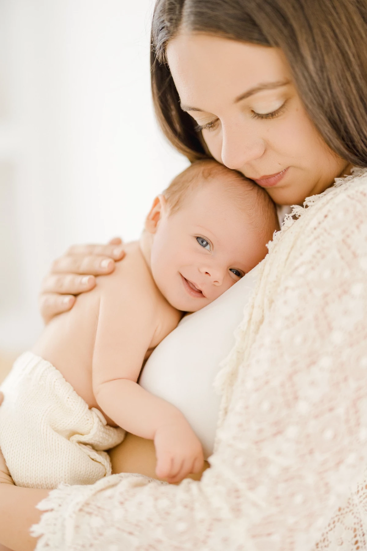 Séance nouveau-né au studio : maman câline son bébé contre elle, peau à peau, dans une lumière douce et naturelle, tendresse infinie