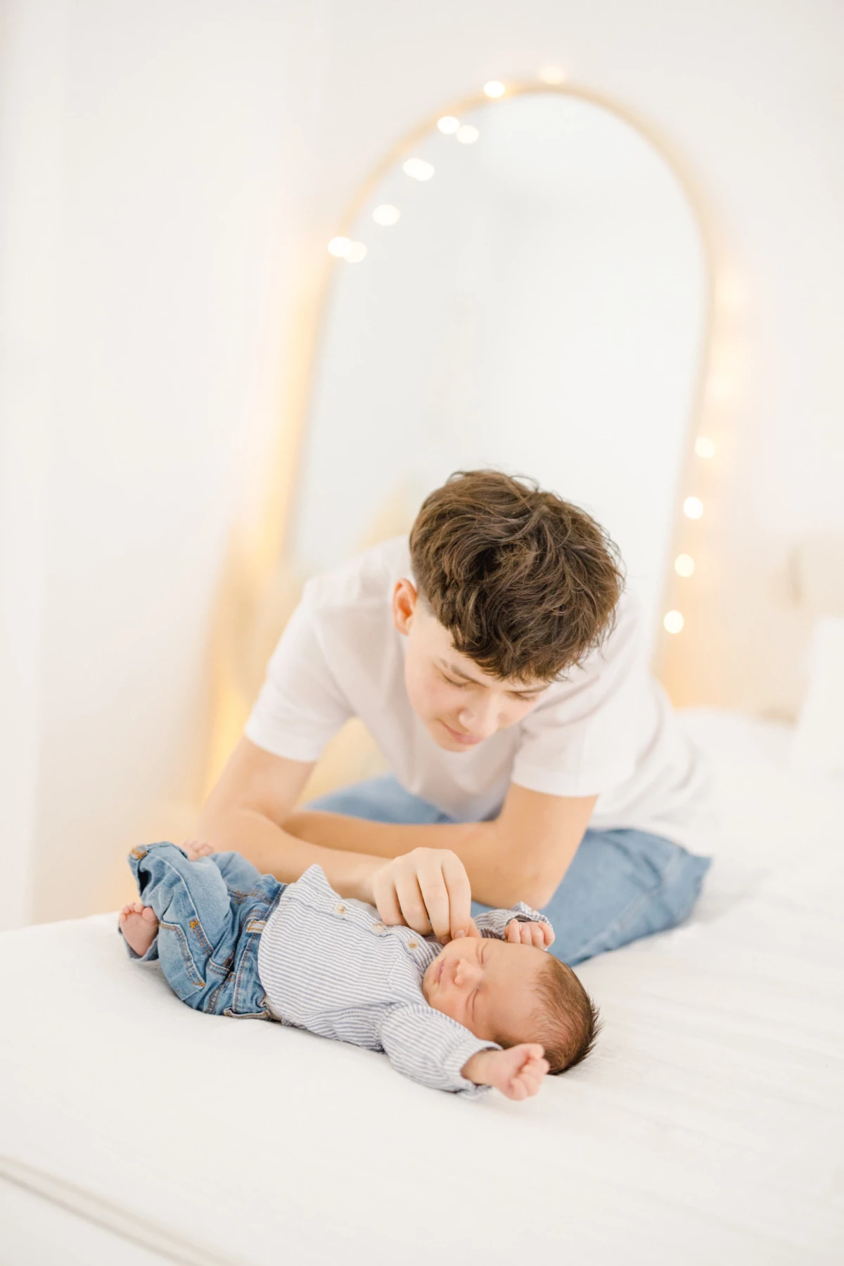 Séance naissance en studio : grand frère veille tendrement sur son petit frère nouveau-né, ambiance douce et lumineuse