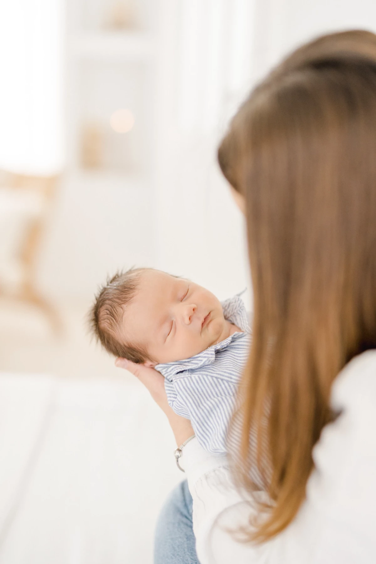 Séance naissance en studio : maman contemple son nouveau-né endormi dans ses bras, instant de tendresse et connexion naturelle