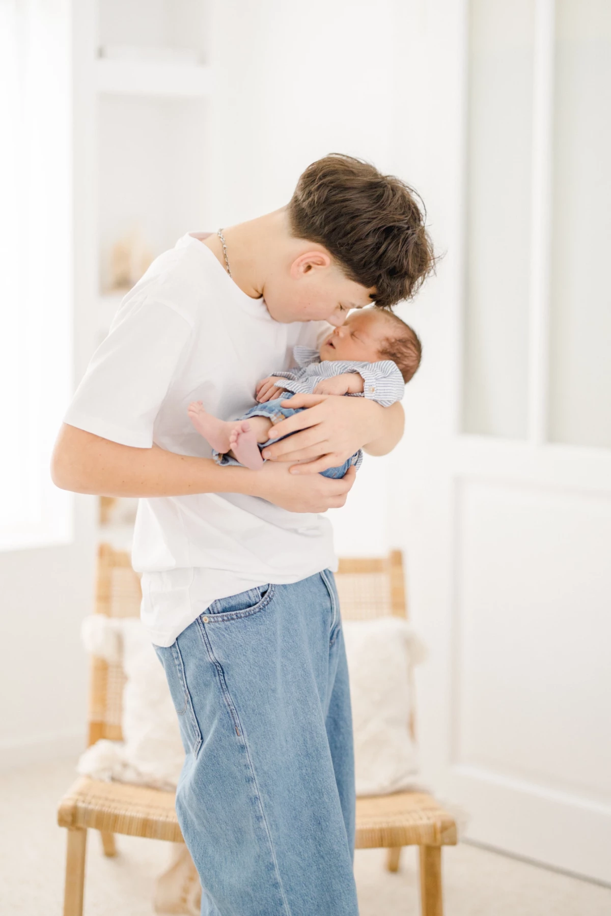 Séance naissance au studio : grand frère embrasse tendrement son petit frère nouveau-né dans ses bras, instant de complicité familiale