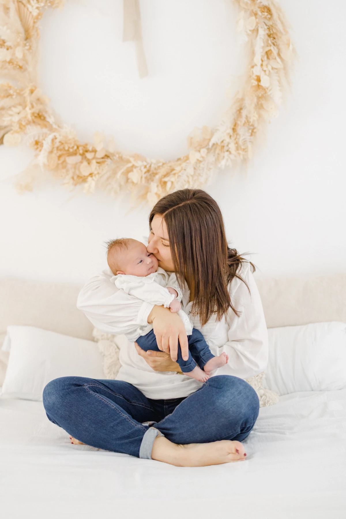 Séance naissance en studio : jeune maman embrasse tendrement son nouveau-né dans une ambiance douce et épurée